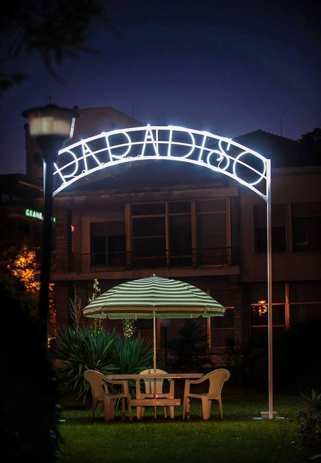 Nighttime outdoor seating area with a table, four chairs, and a striped umbrella, under a lit sign reading 'DARIA BISTRO'.
