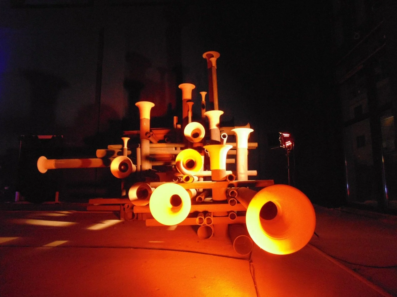 A sculpture made of various pipes and tubes illuminated by orange glowing lights in a dark space.