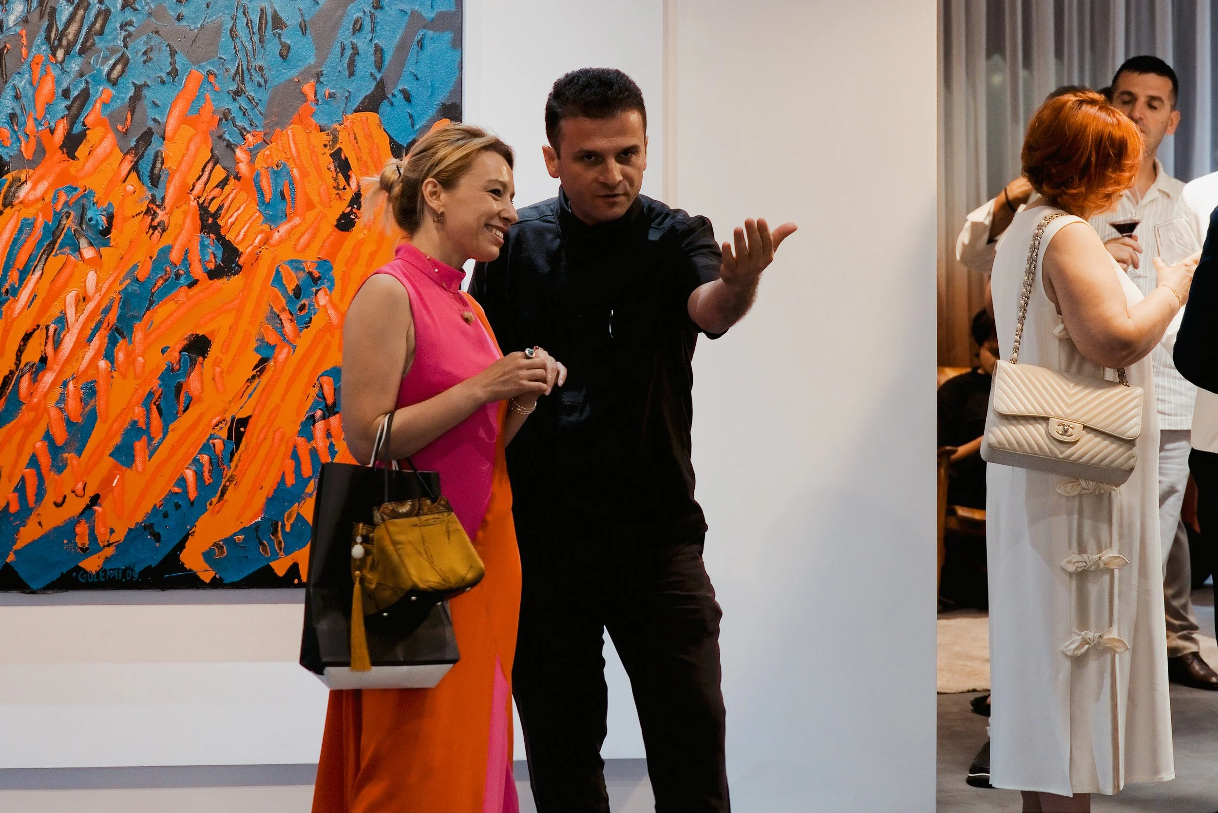 People at an art gallery, chatting near colorful abstract paintings on the wall.