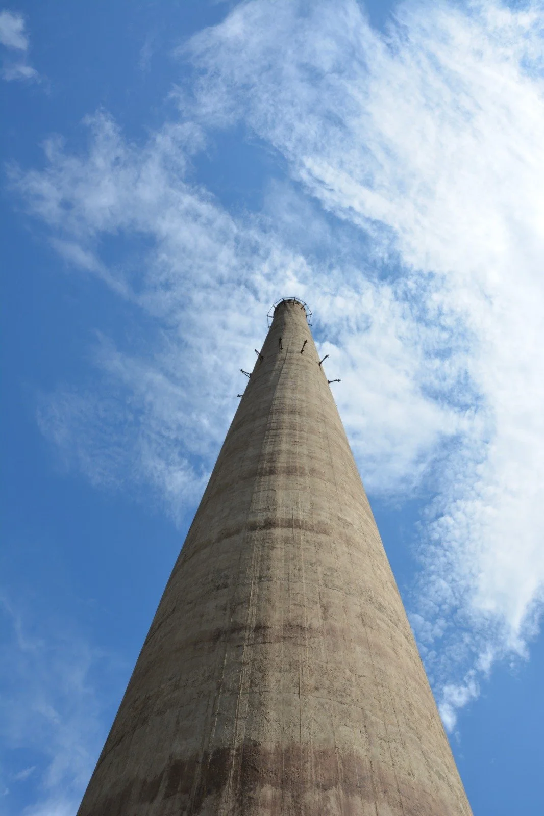A tall industrial chimney reaching up toward a partly cloudy blue sky.