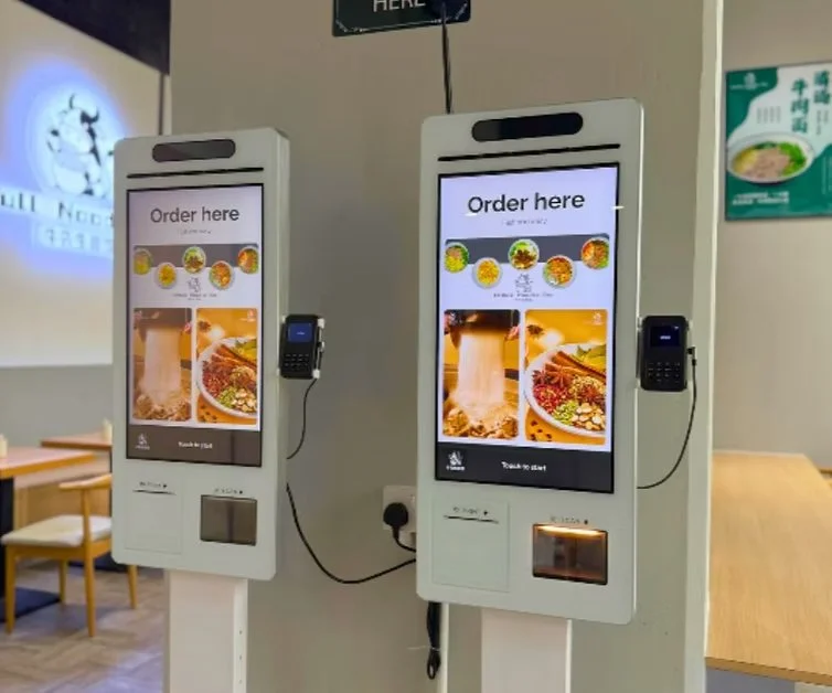 Two self-order kiosks with touch screens in a restaurant.
