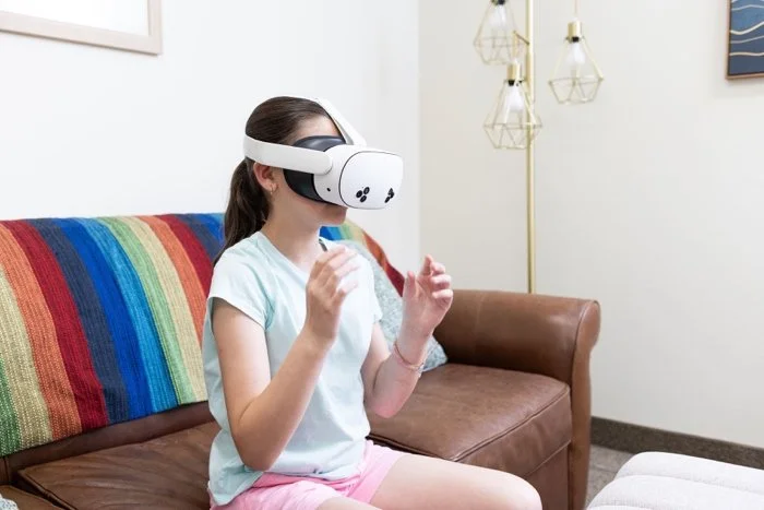 Girl patient wearing a virtual reality headset sitting on a couch with a rainbow-striped blanket.