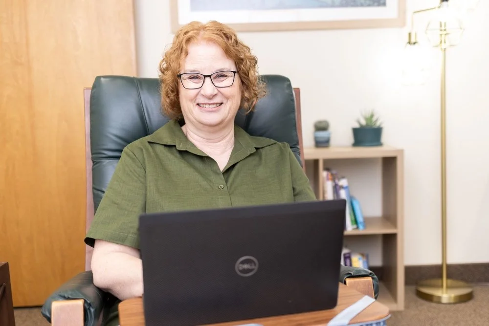 Karen sitting at a desk with a black laptop, smiling.