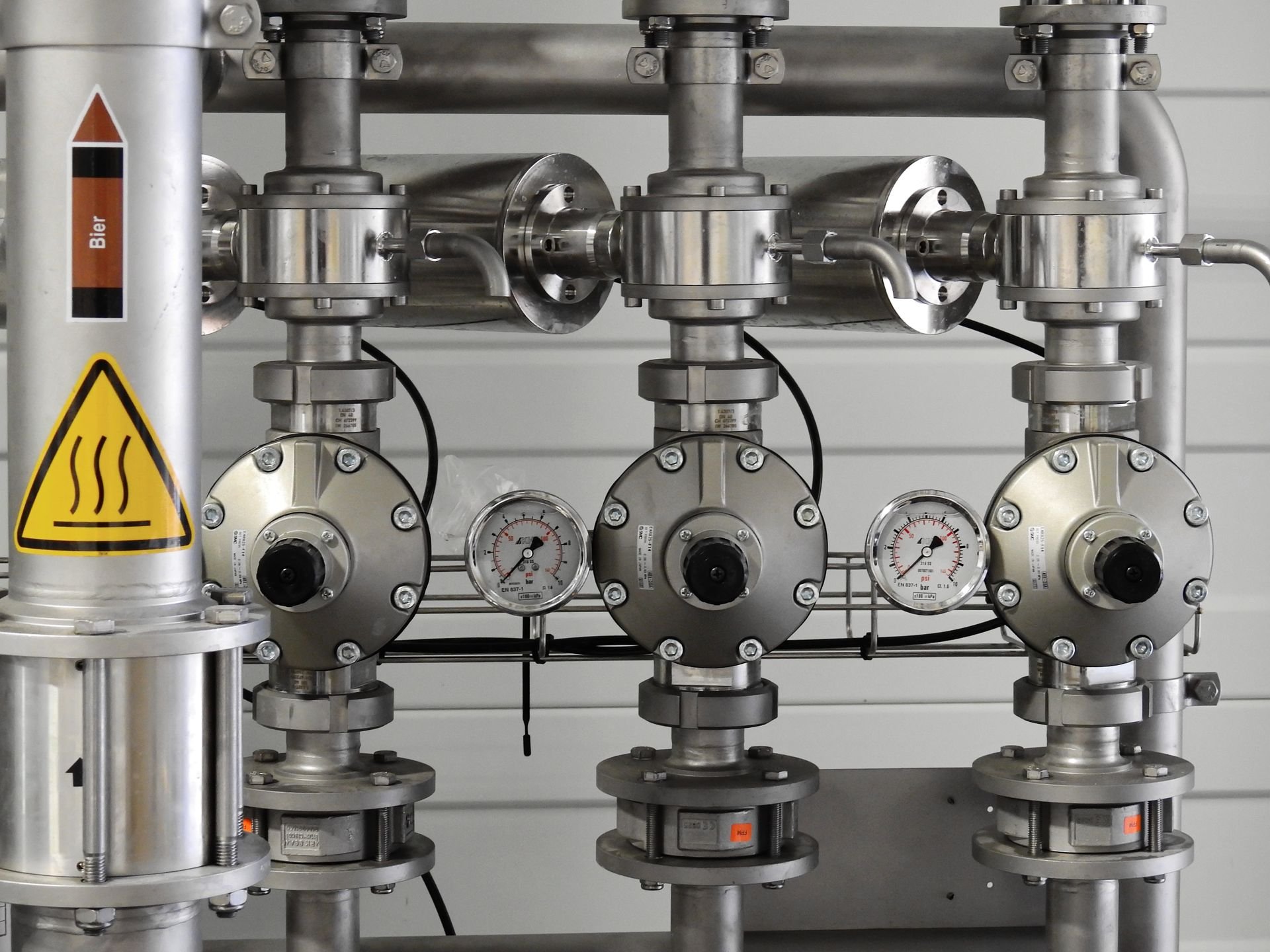 Industrial stainless steel piping system with gauges, valves, and warning labels.