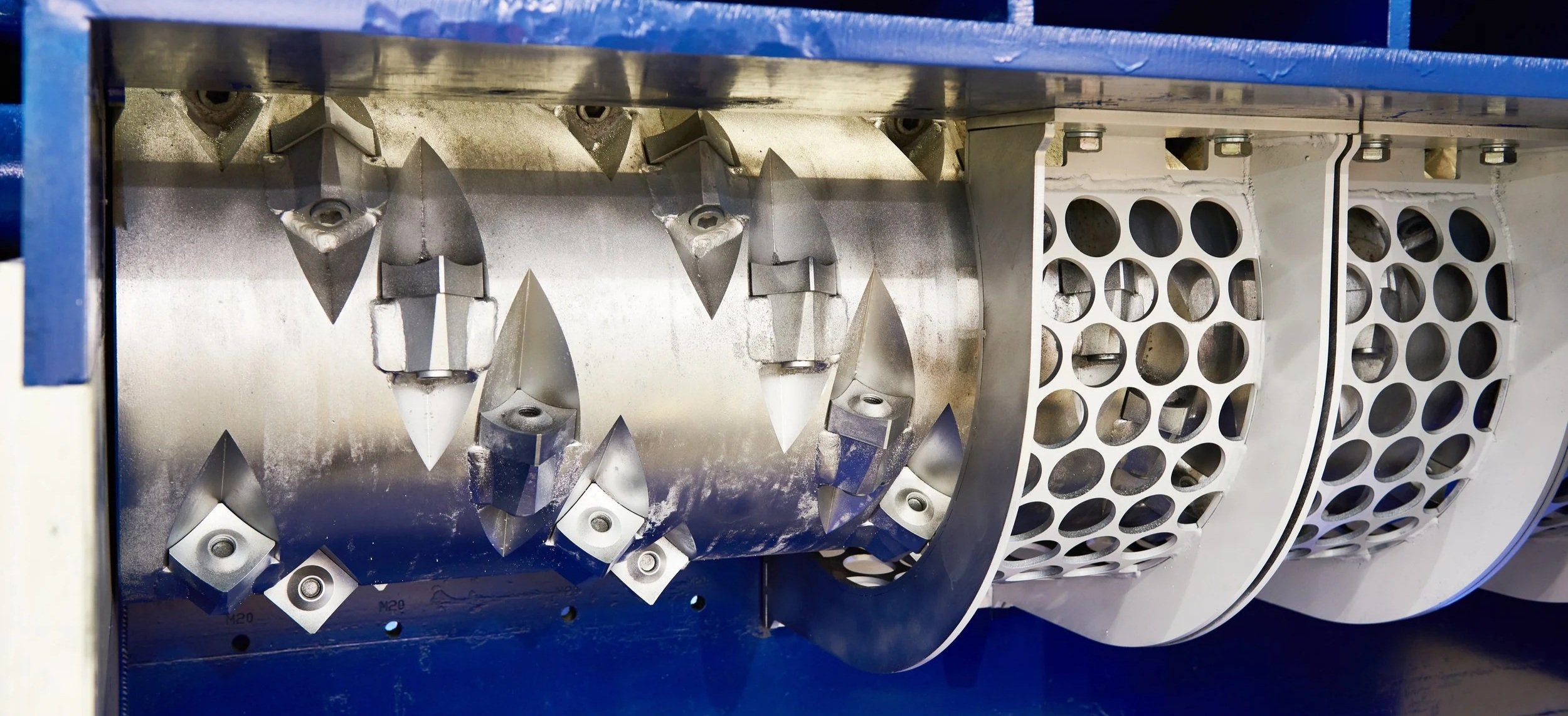 Close-up of a metal machine component with sharp-edged blades and perforated white cover.
