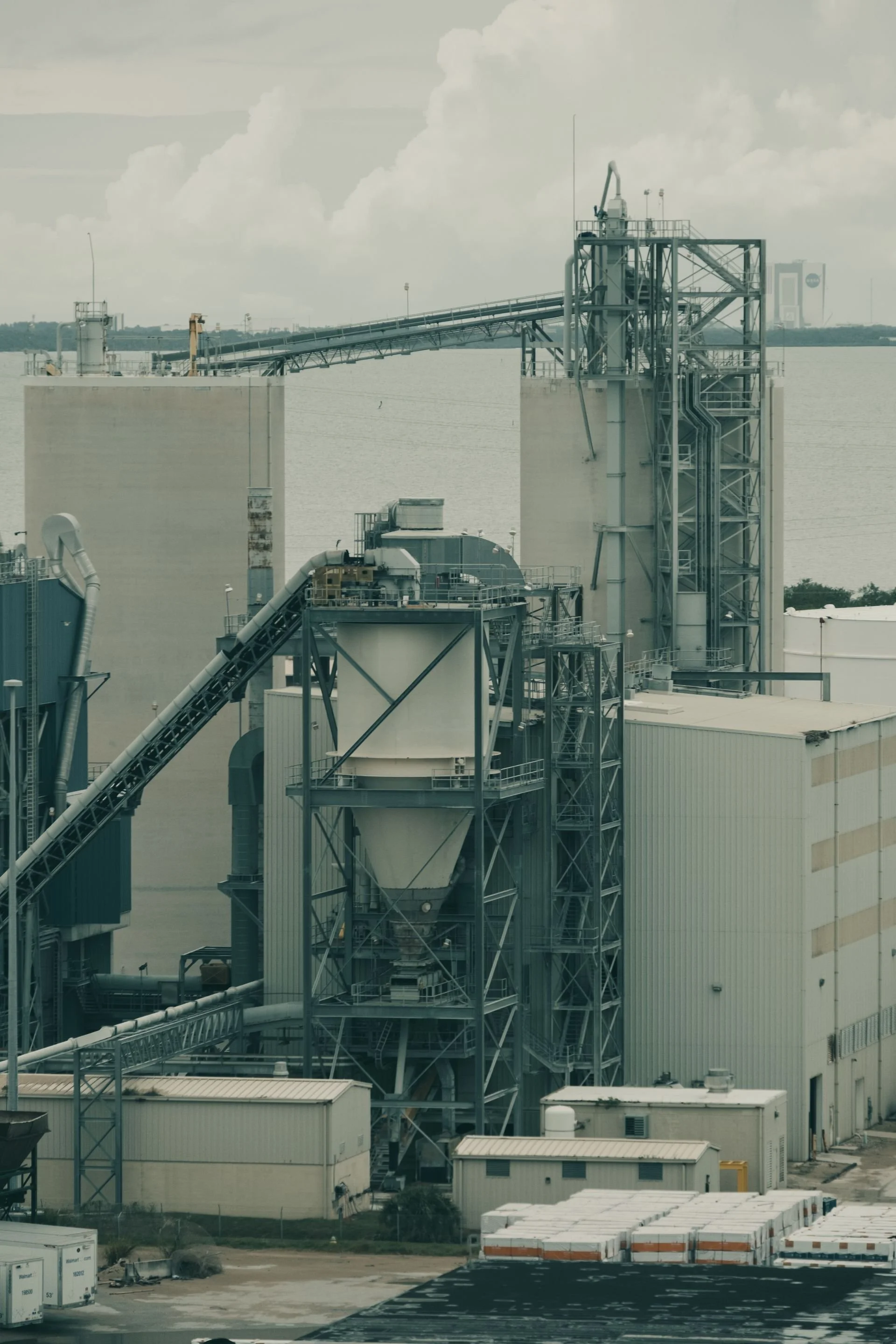Industrial facility with piping, and structural framework, with storage containers and equipment in the foreground.