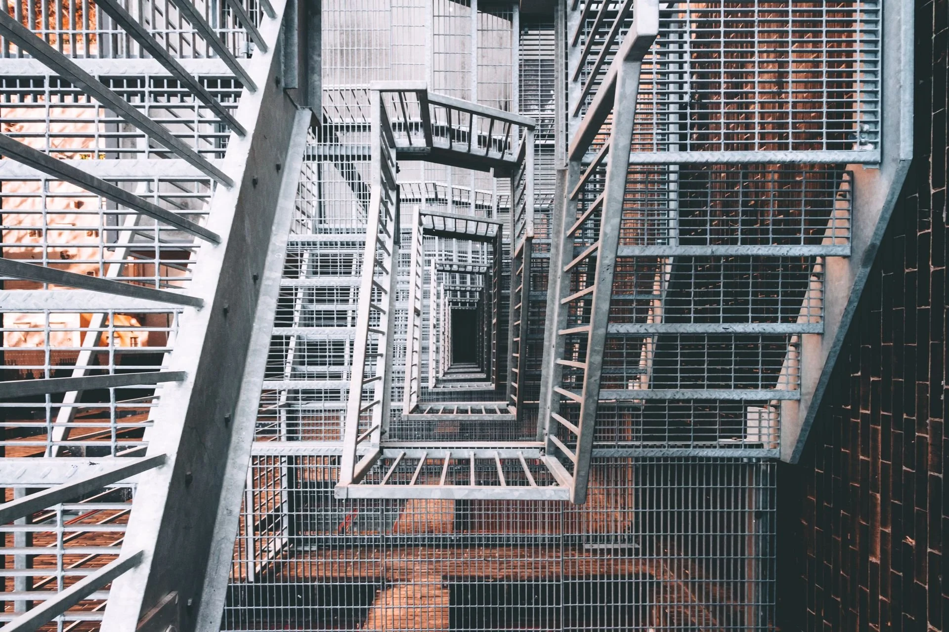 Looking down on a tall, metal staircase with grated steps and railings, spiraling downward in a square pattern.