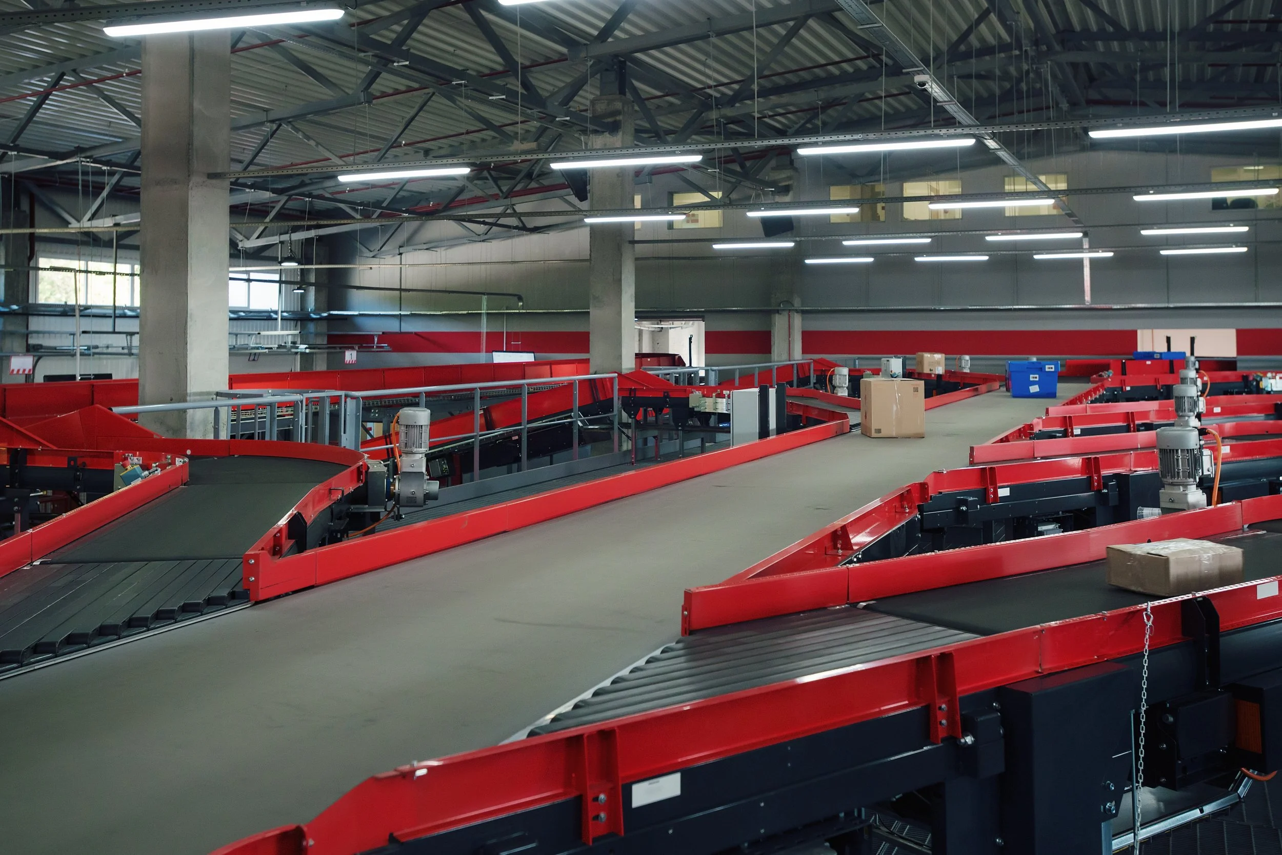 An empty industrial conveyor belt system with red frames and rollers inside a warehouse or factory.