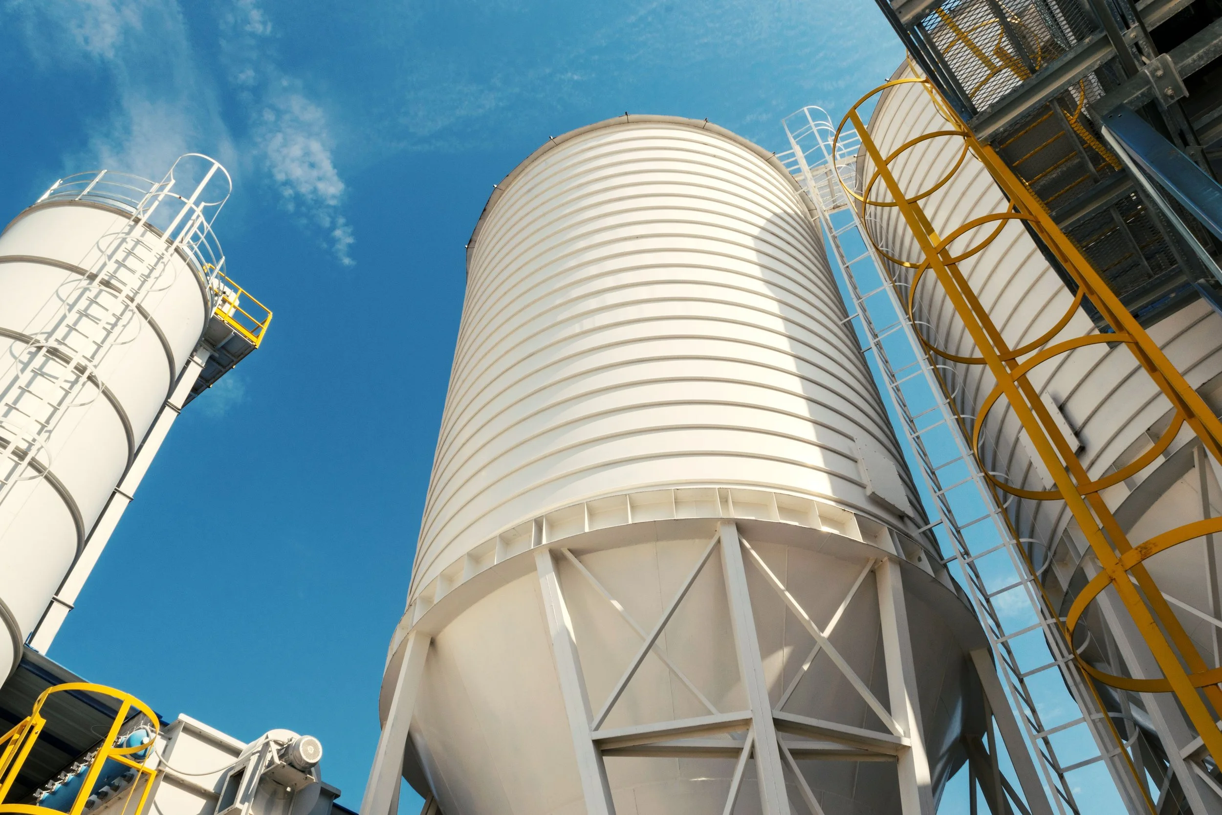 Industrial storage tanks with ladders and railings against a blue sky.