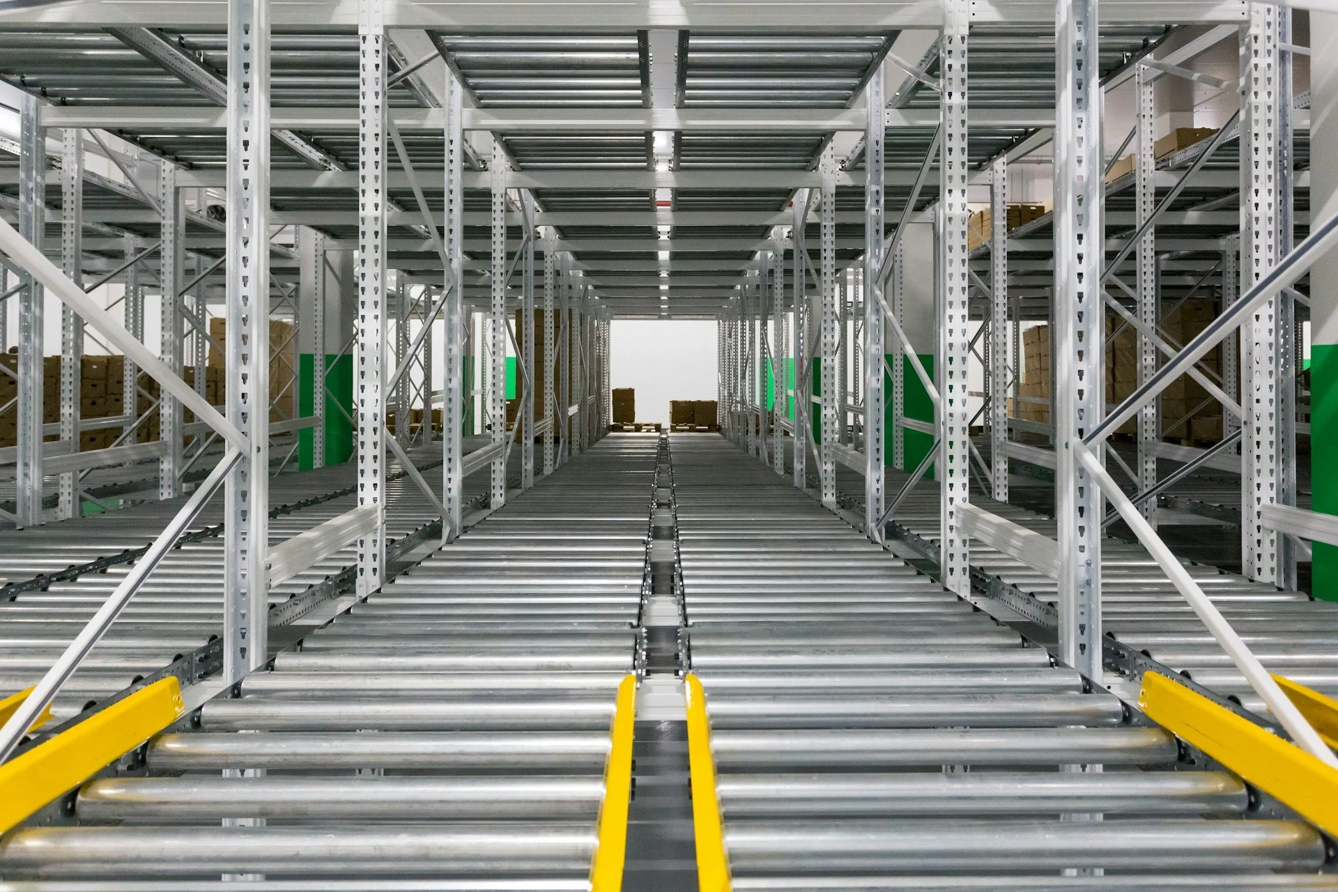 Empty warehouse with metal shelves on both sides and metal roller tracks on the floor for trolley movement.