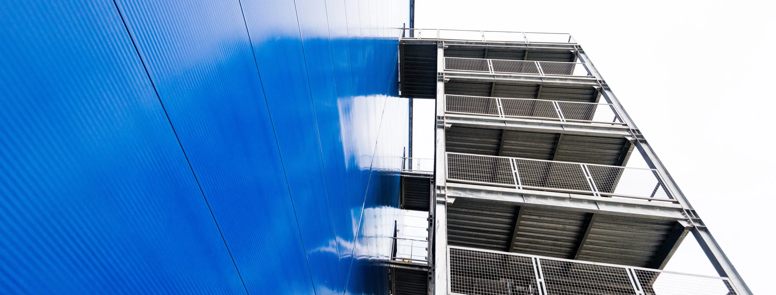 Exterior view of a modern building with blue panels on one side and metal fire escape stairs with railings on the other side