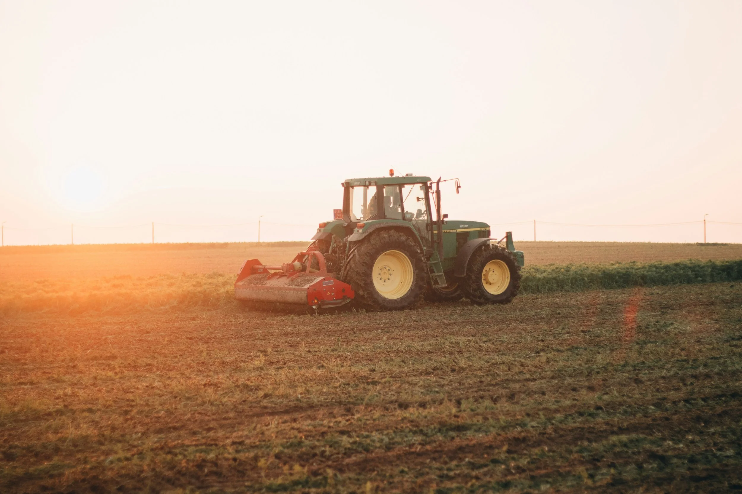 A green tractor with yellow wheels working in a field at sunset.