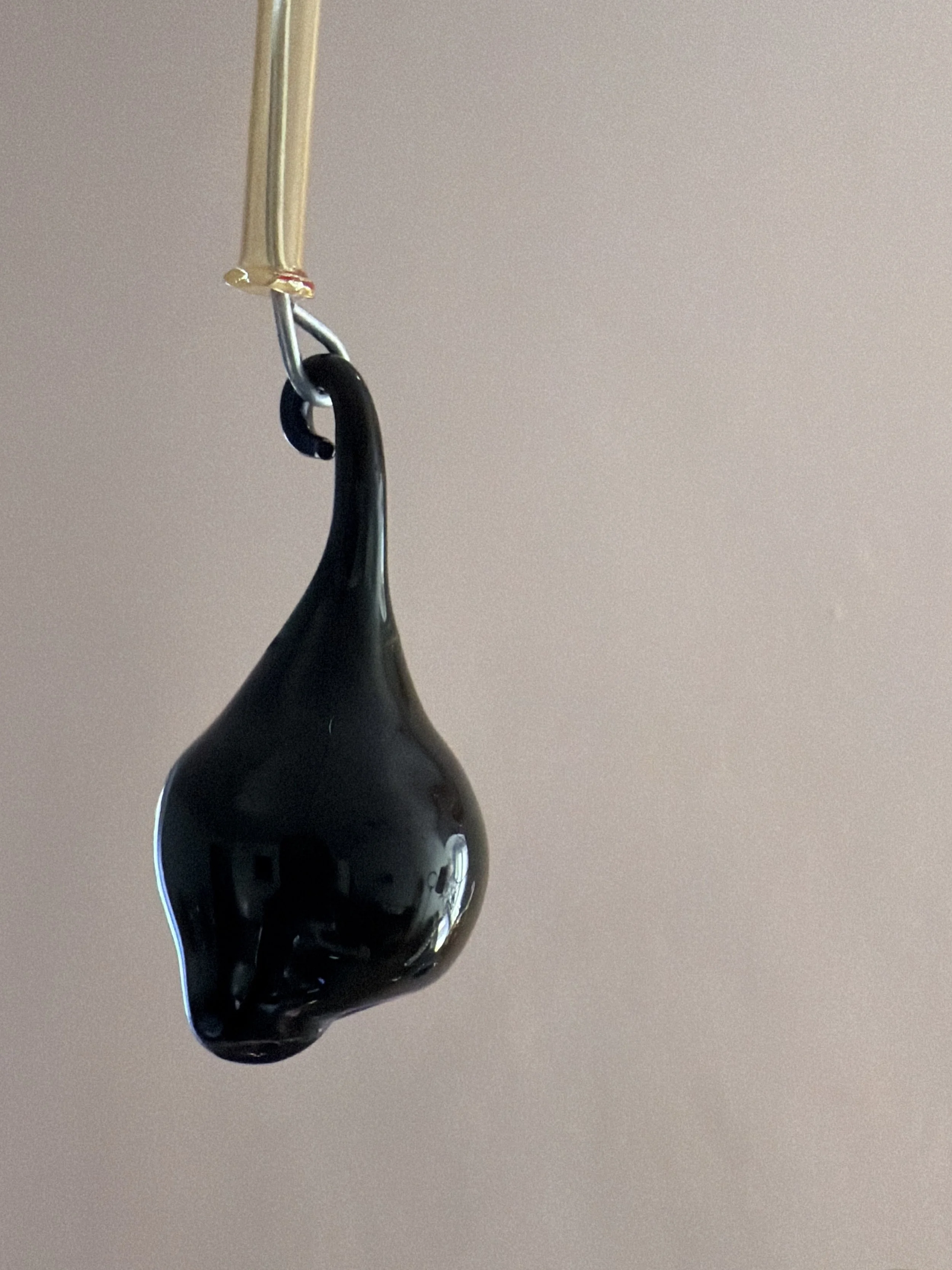 Schwarzer Wassertropfen hängt an einem güldenen Rohr vor einem hellen Hintergrund.