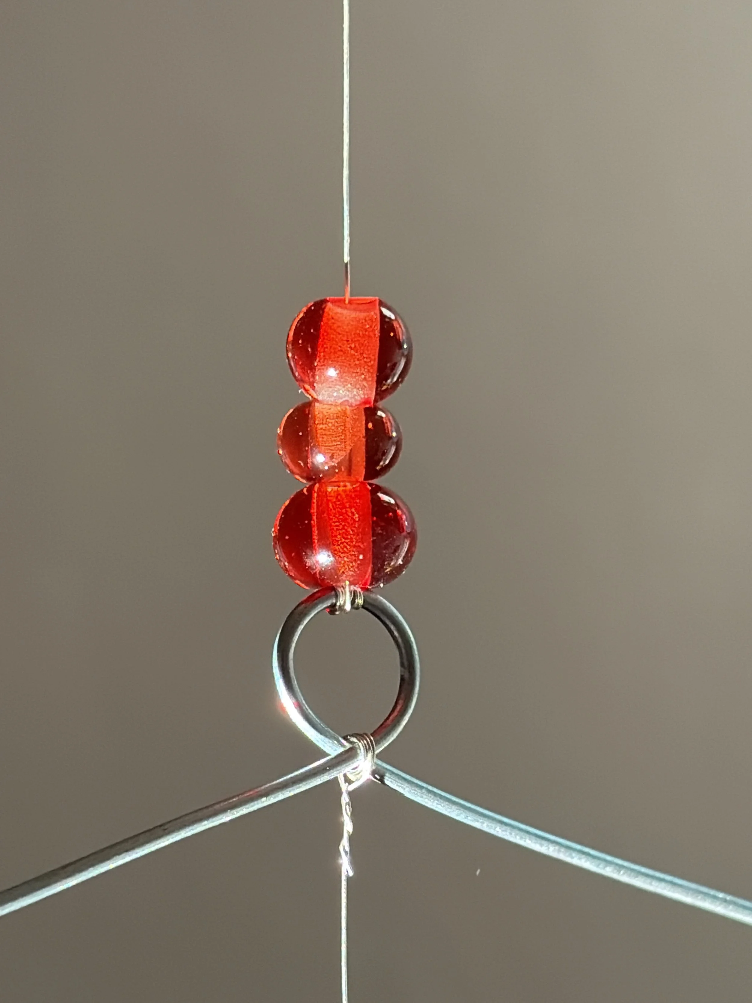 Nahaufnahme eines roten und transparenten Gegenstands, der an einer silbernen Metallstruktur befestigt ist, mit einer grauen Wand im Hintergrund.