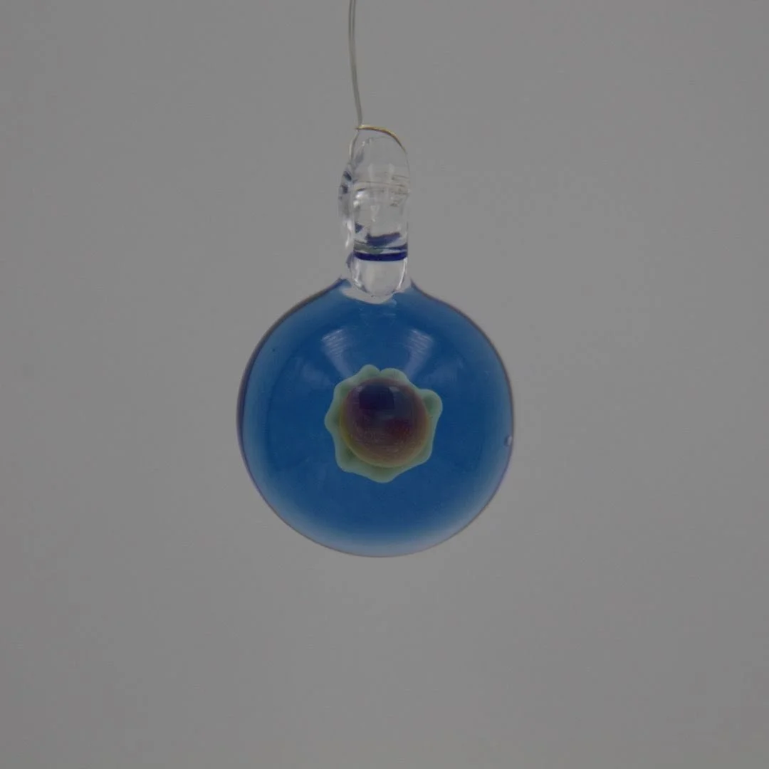 Runder handgefertigter Glasanhänger aus blauem Borosilikatglas mit hellem Blütenmotiv in der Mitte