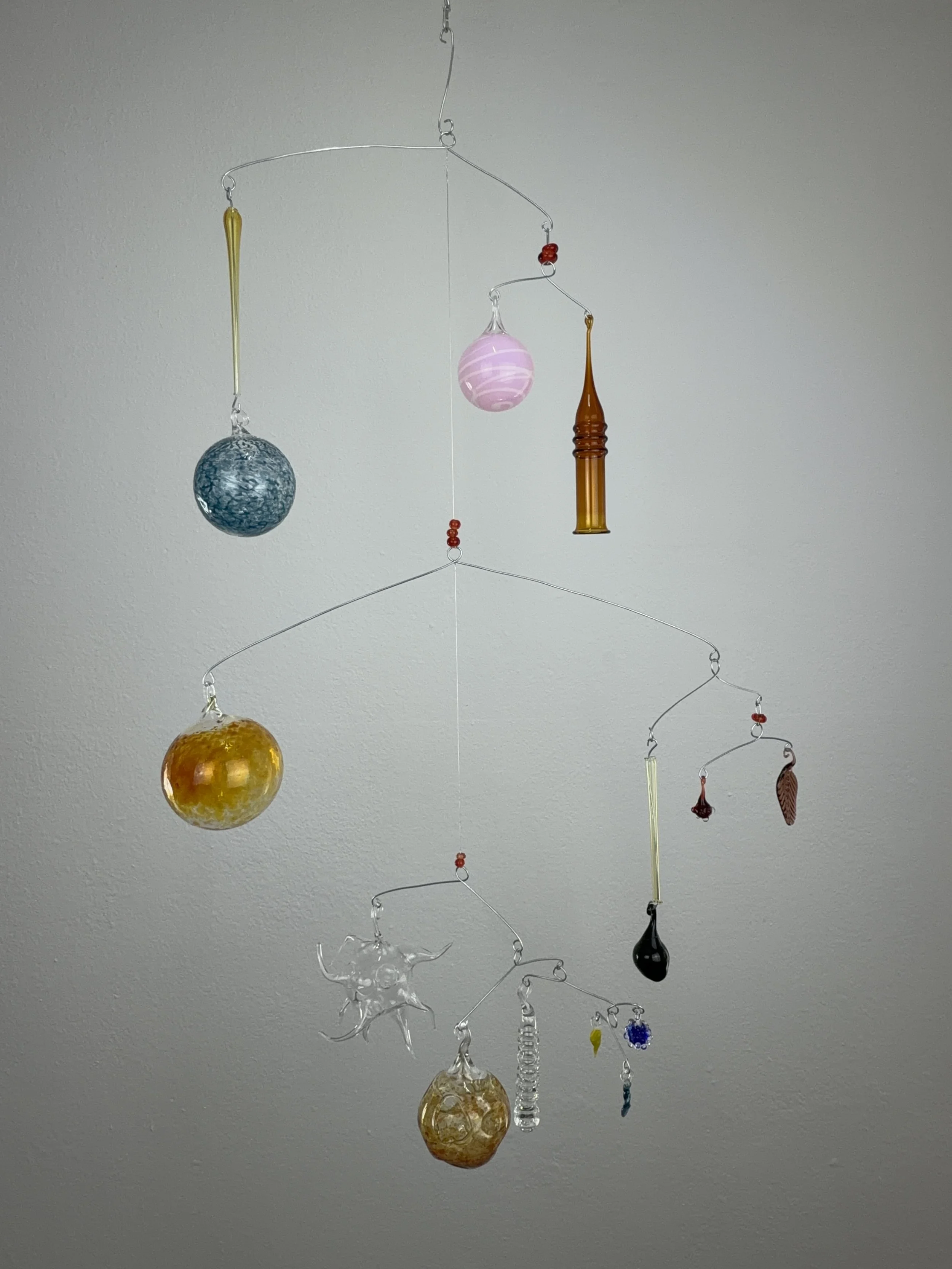 Glas-Mobile mit mehreren bunten Anhängern vor weißer Wand, StudioJoshi