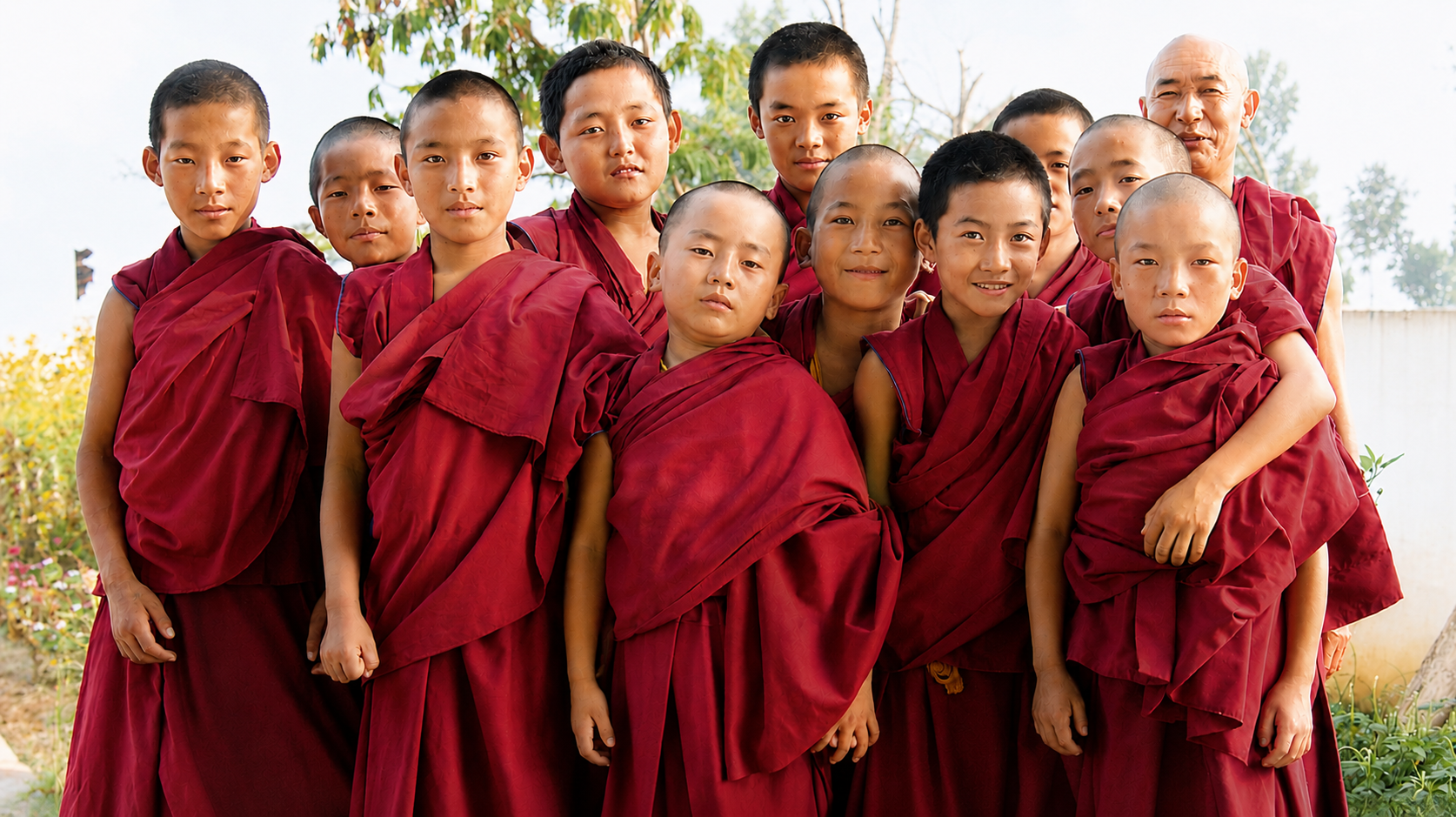 Een groep jonge monniken in rode robes, samen poseerend buiten.
