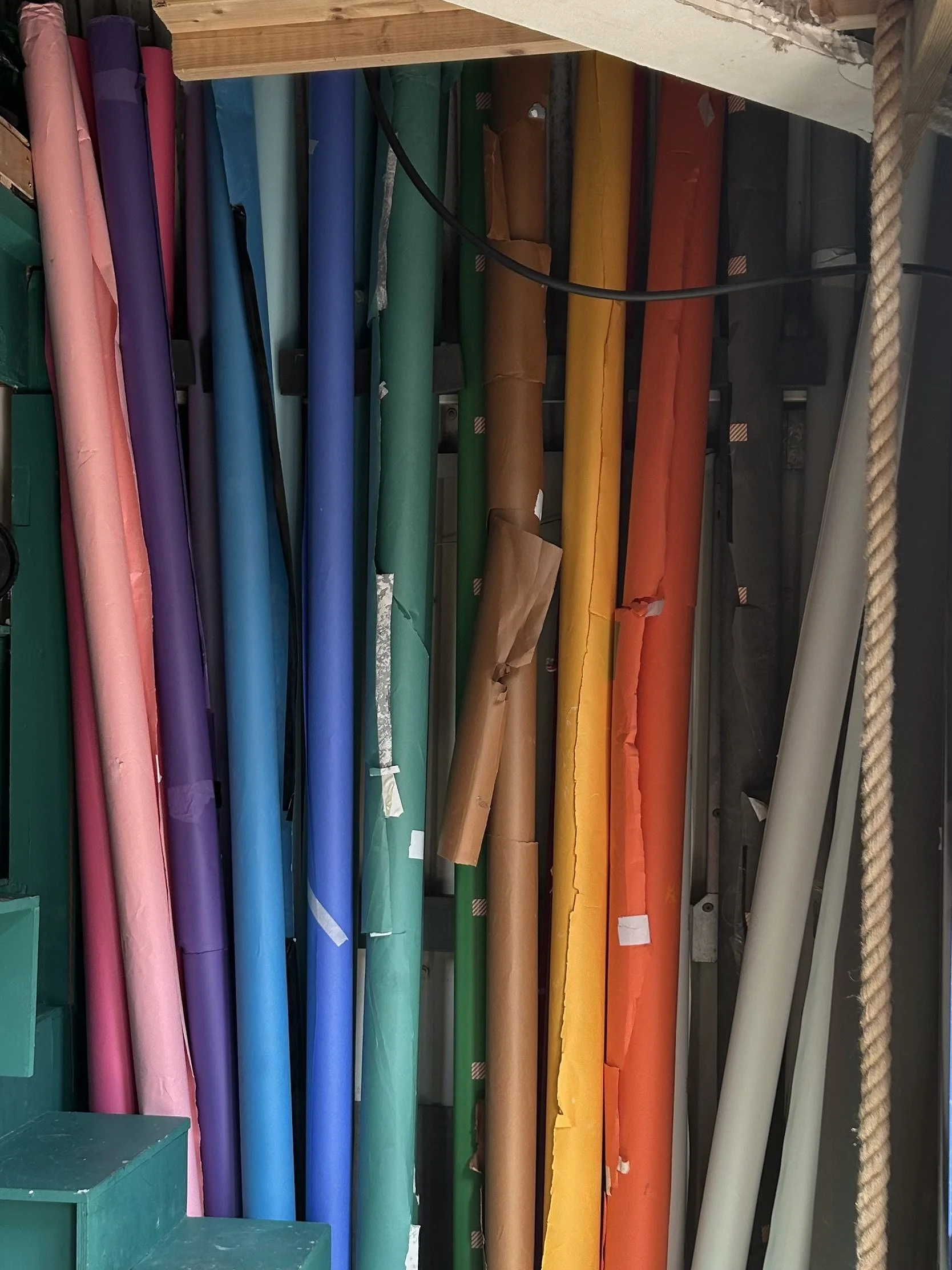 Colorful rolls of wrapping paper organized by color on a display shelf, with a beige rope on the right side.