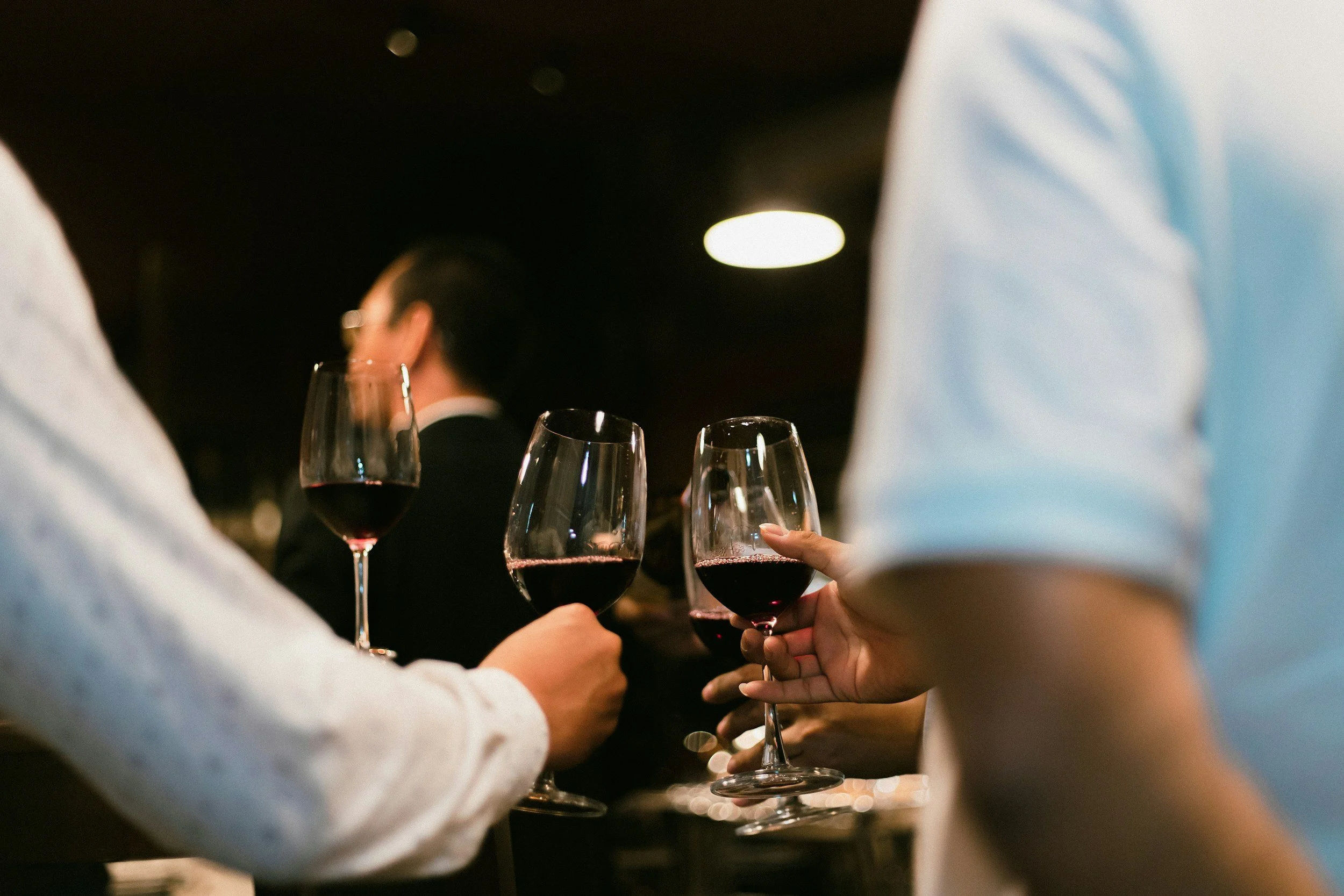 People holding glasses of red wine at a social gathering or celebration.