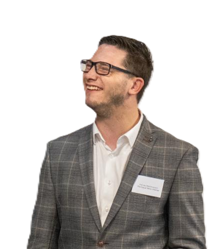 Harvey Matthewson smiling and wearing glasses, a gray plaid suit, and a name tag at a professional speaking event.