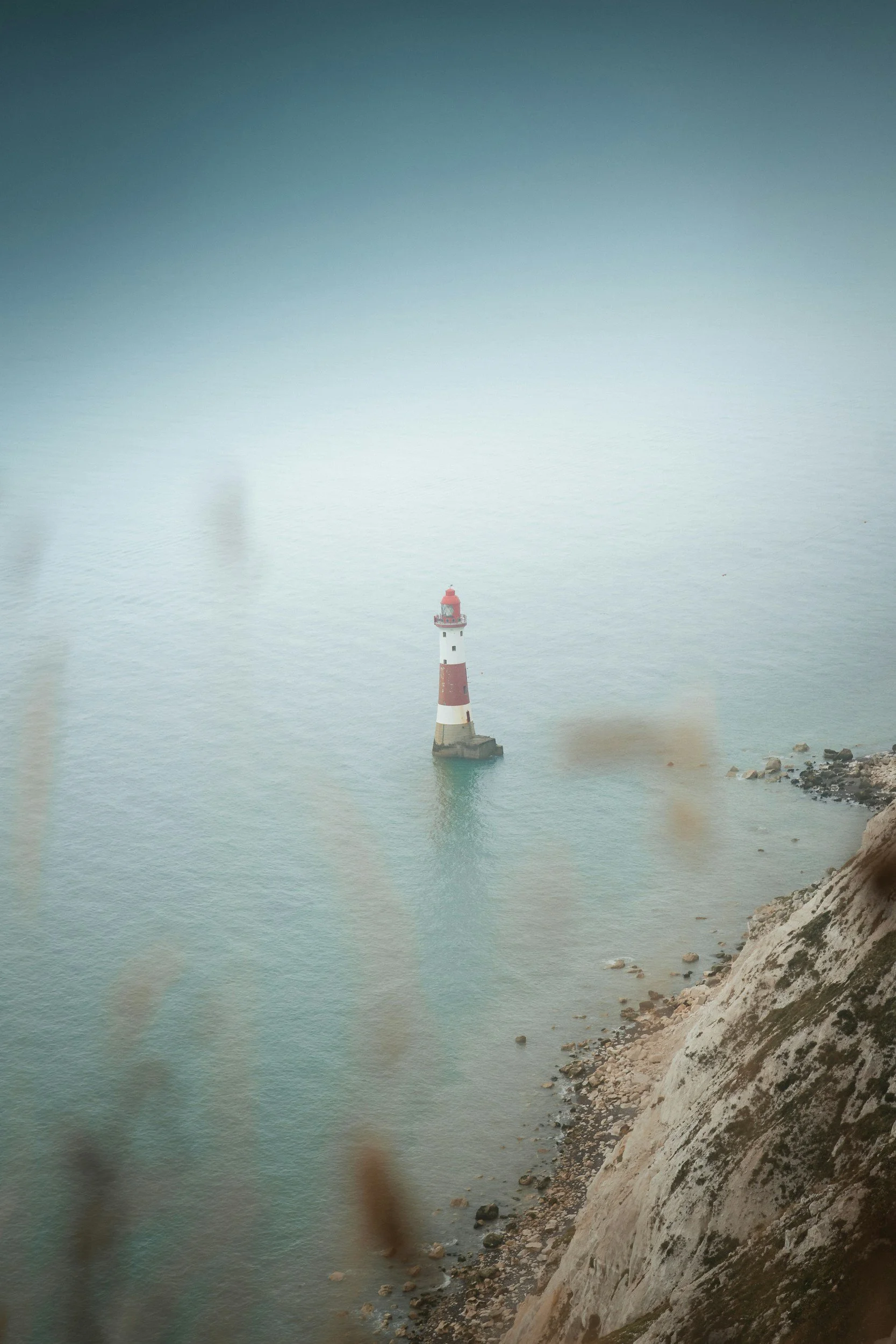A lighthouse standing on a rocky shoreline with calm water and white chalk cliffs in the background.