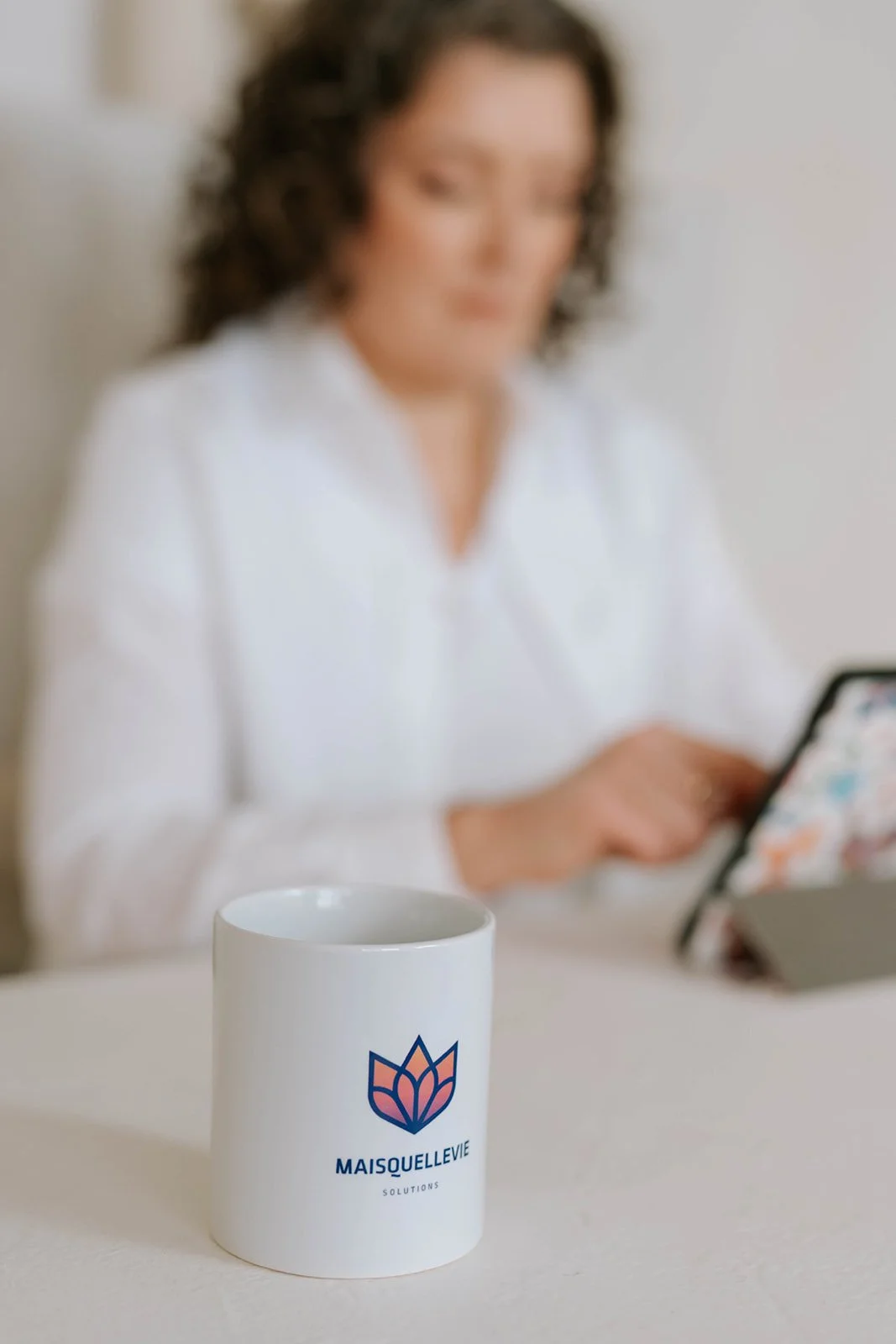 Mais Quelle Vie Solutions coffee mug in the foreground with Marie-Claire McKelvey working on a tablet in the background.