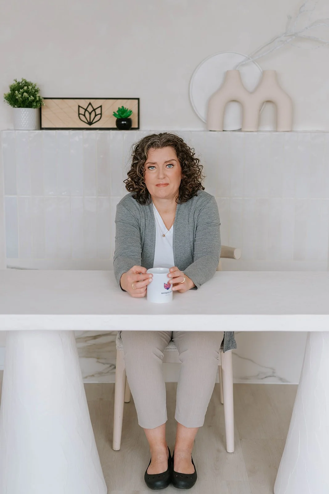Marie-Claire McKelvey sitting at a table holding a coffee mug in her home workspace, reflecting on resilience, writing, and advocacy.