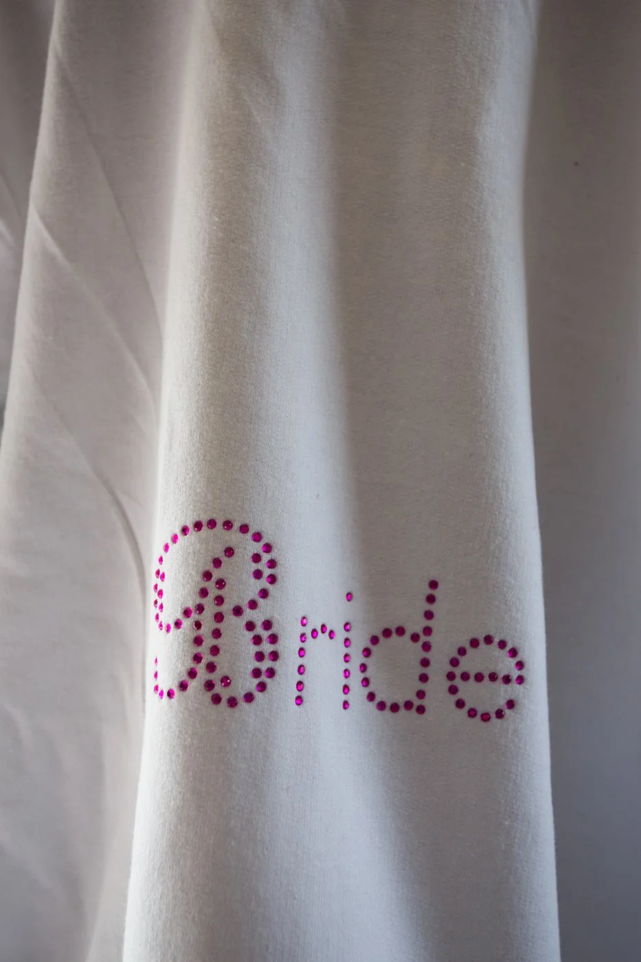 White fabric with the word 'Bride' spelled out in pink rhinestones.