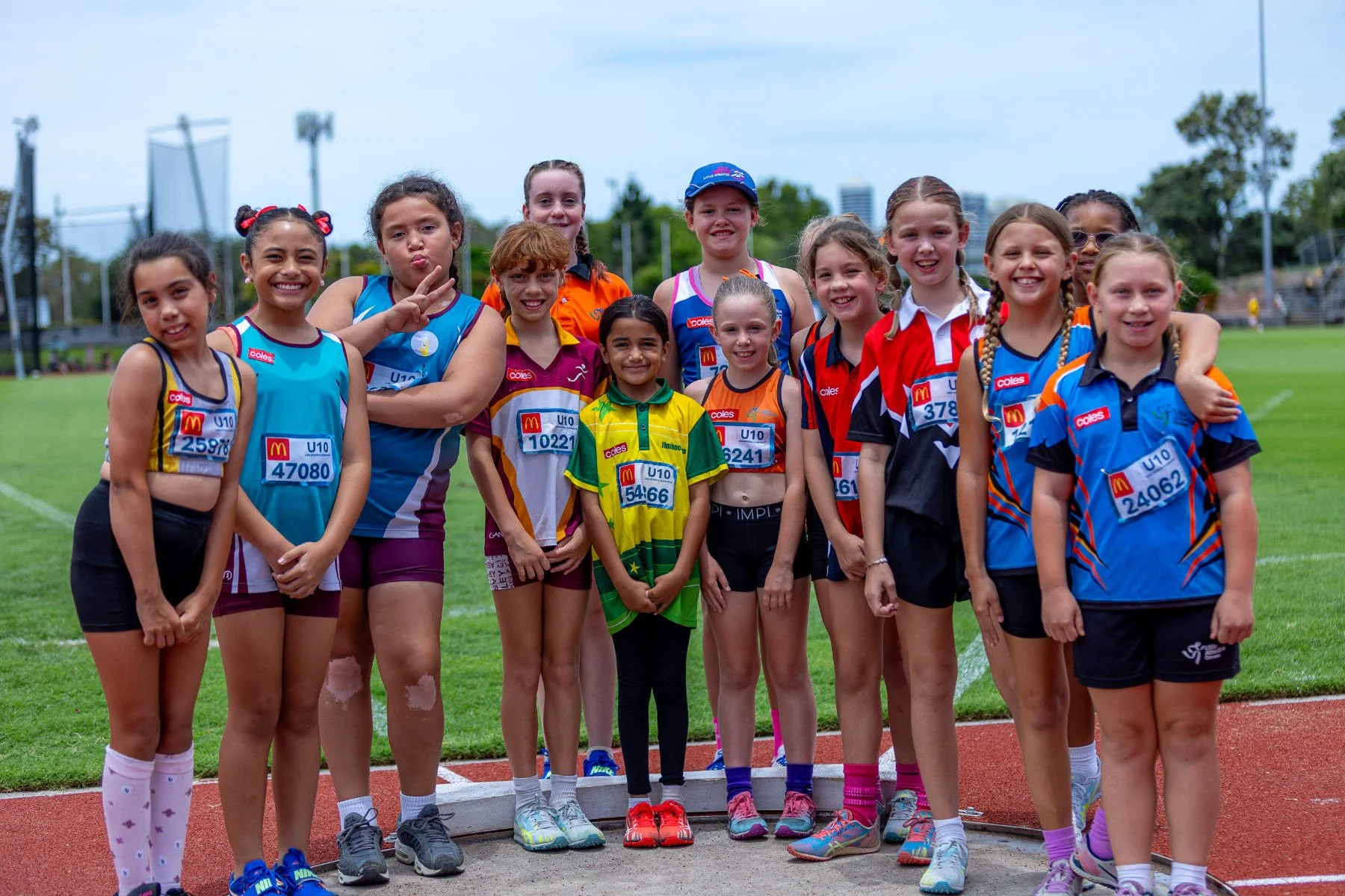 Group of young female athletes in colorful sports uniforms, standing together on an outdoor track, smiling and posing for the photo.
