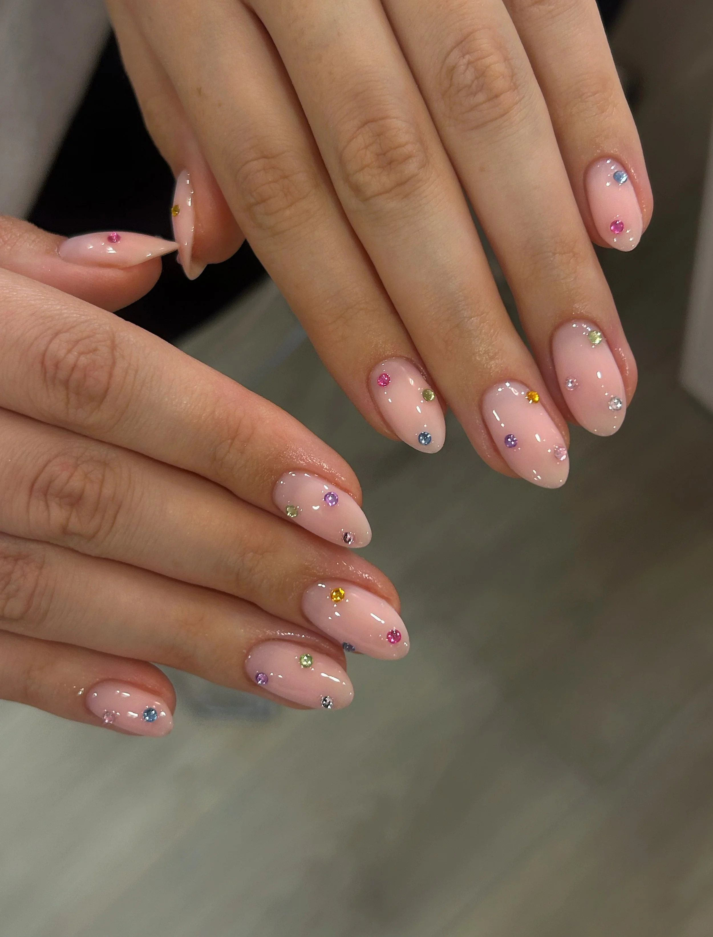Close-up of a person's hand with neatly manicured nails painted in a light pink color, decorated with small multi-colored rhinestones.