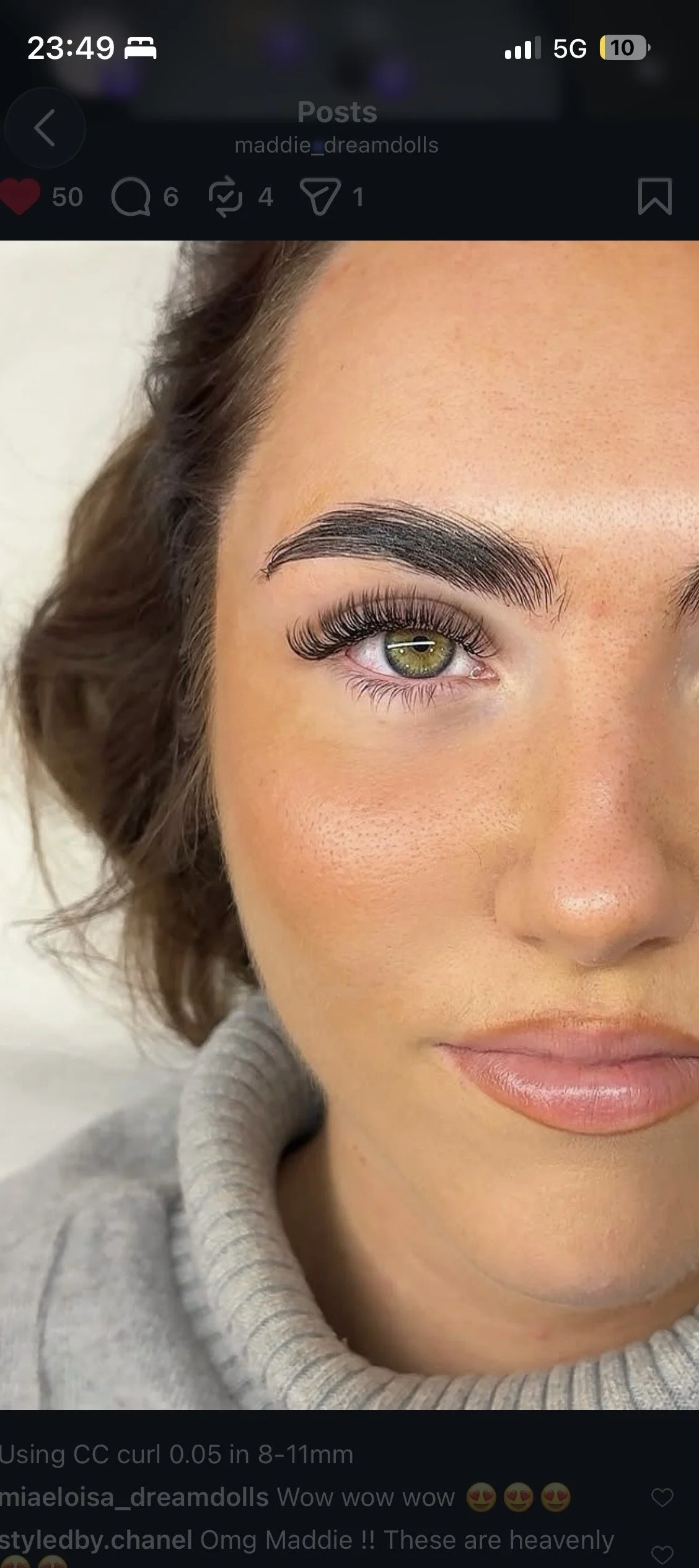 Close-up of a woman with light skin, green eyes, brown hair, full eyebrows, and long eyelashes, wearing a gray turtleneck sweater.