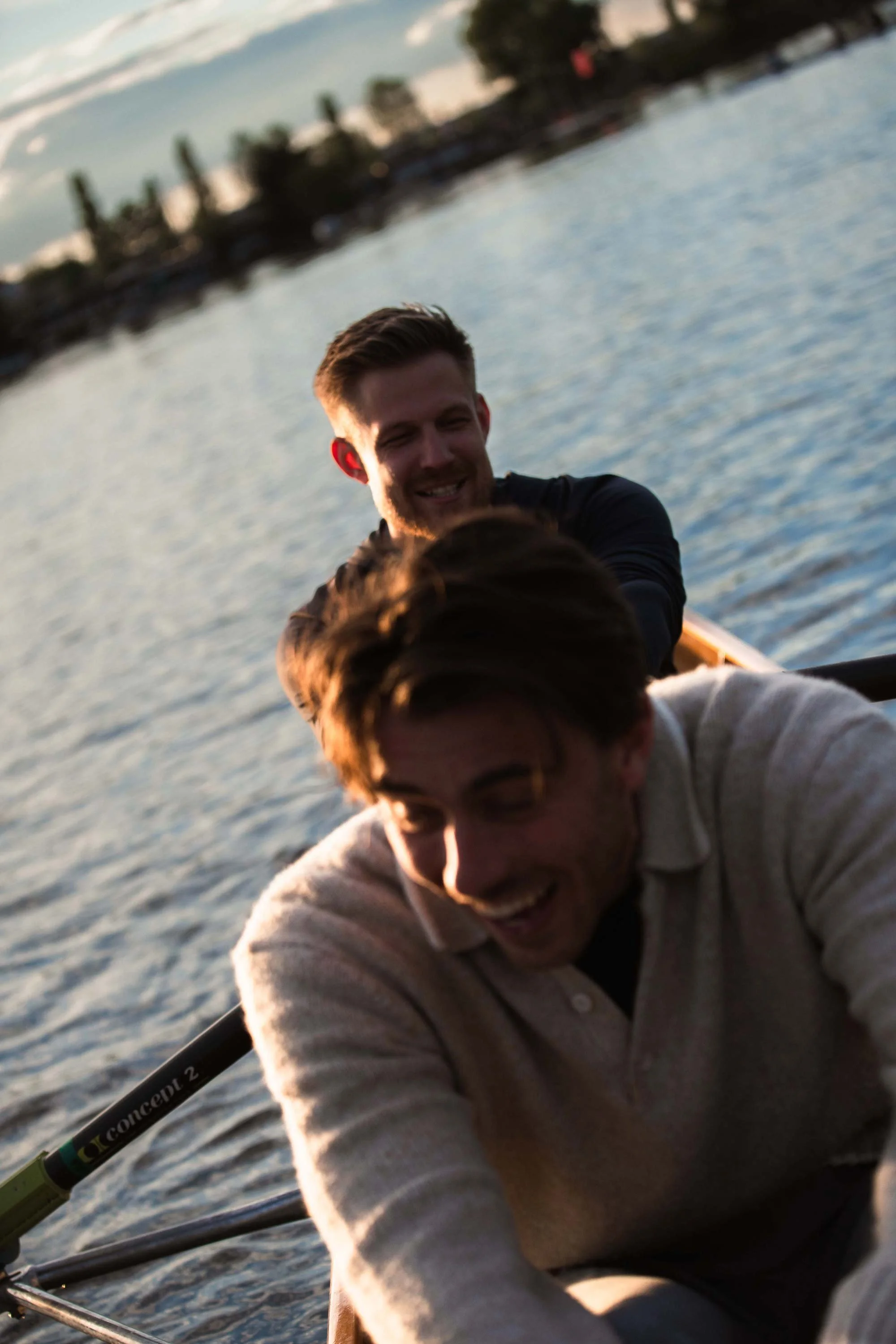 Zwei junge Männer, die im See ein Boot rudern, bei Sonnenuntergang, lachend und Spaß habend.