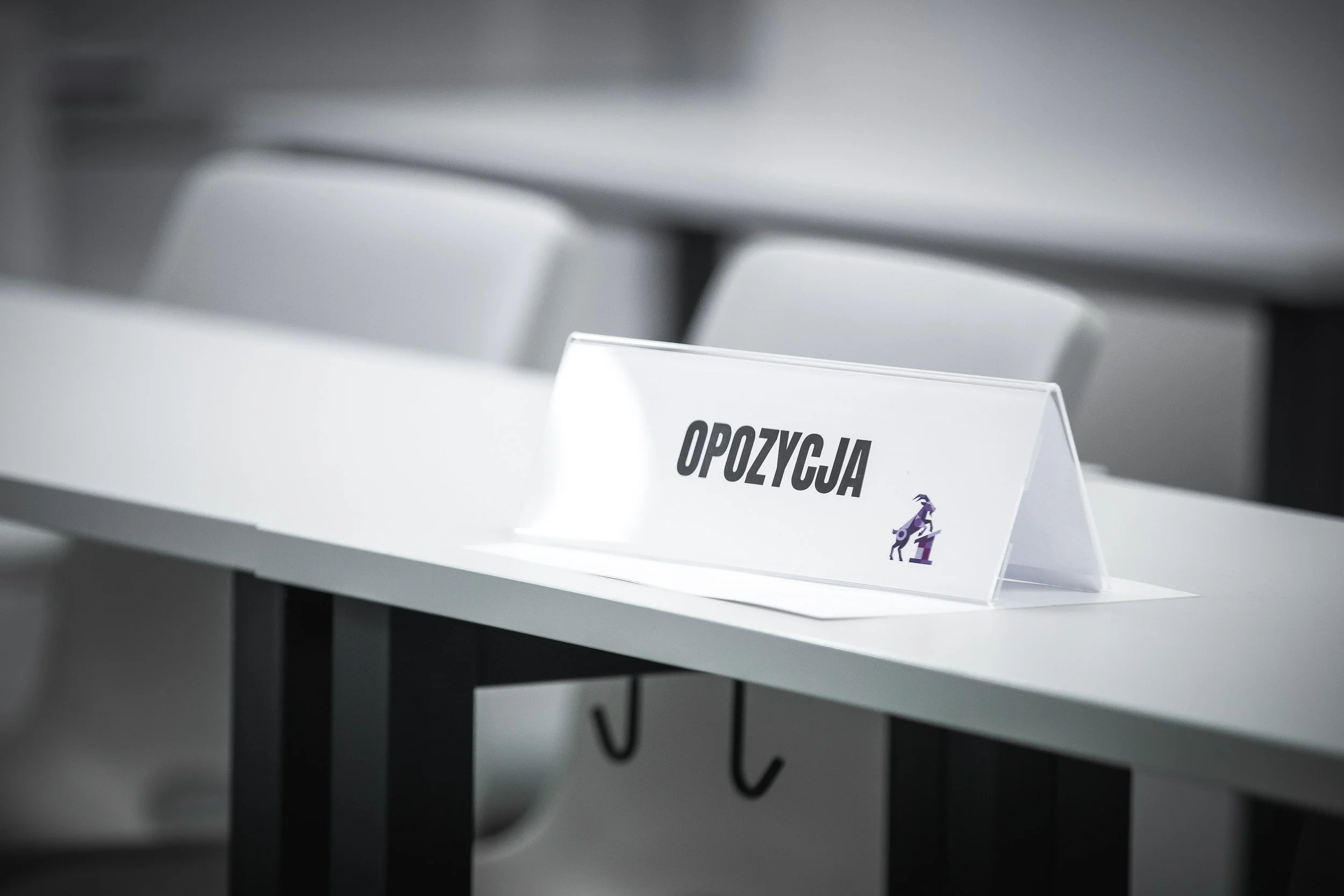 A nameplate on a desk with the word 'OPOZYCJA' and an illustration of a goat riding a motorcycle.