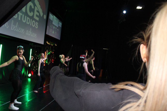 A woman taking a photo of a group of dancers on stage at a studio.