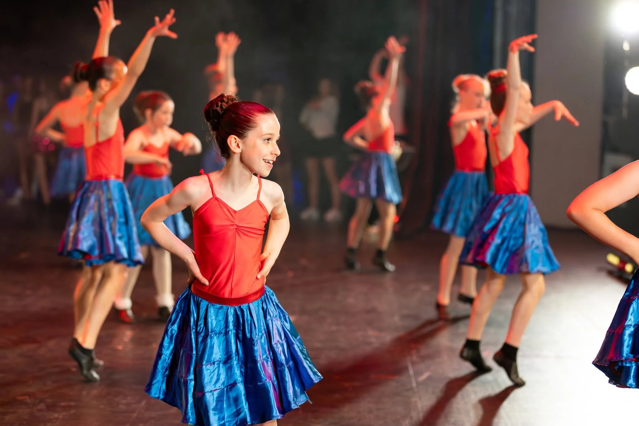 A group of young girls dressed in red and blue costumes performing a dance on stage.