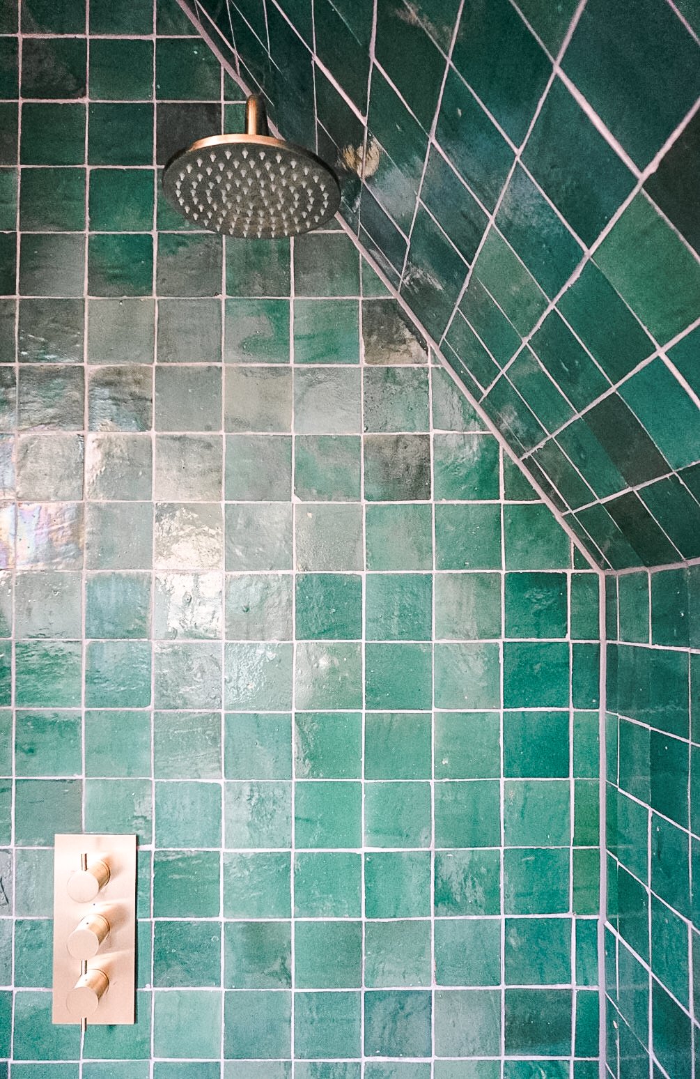 Groene betegelde douche met regendouchekop en een witte thermostaatknop