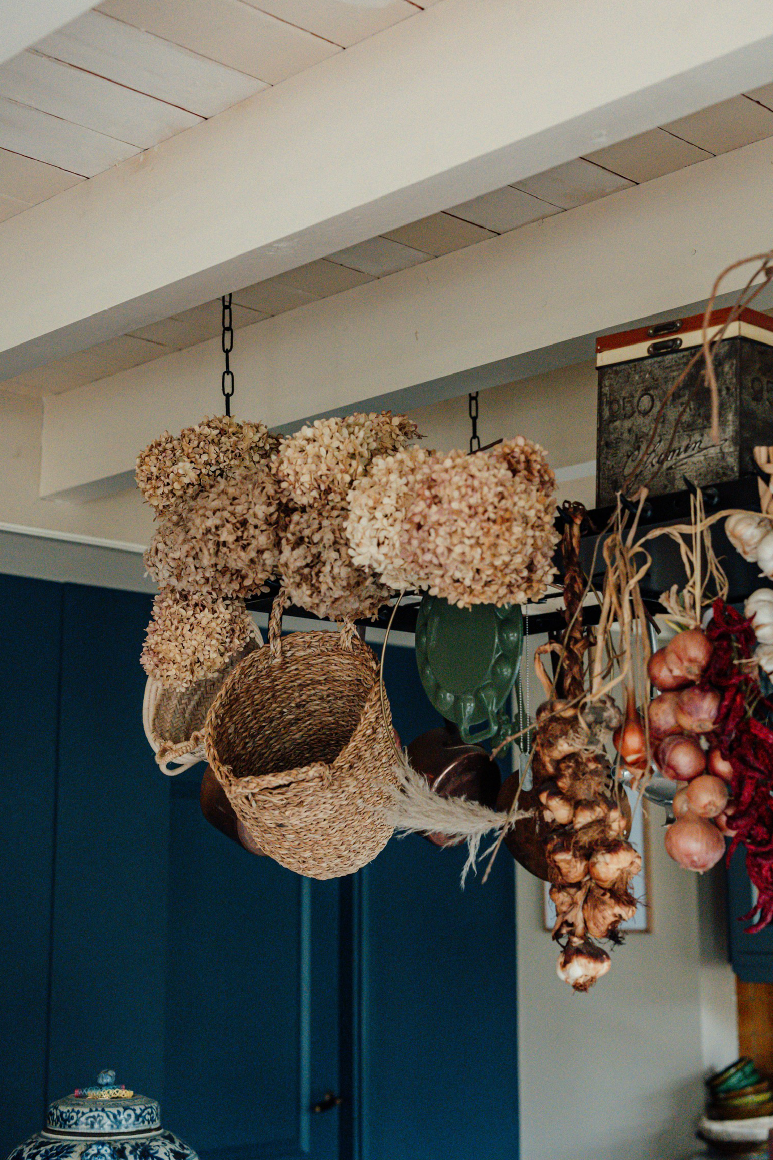Droogboeket met gedroogde bloemen, gerolde en geweven manden, in een interieur met blauwe kast en keramiek.