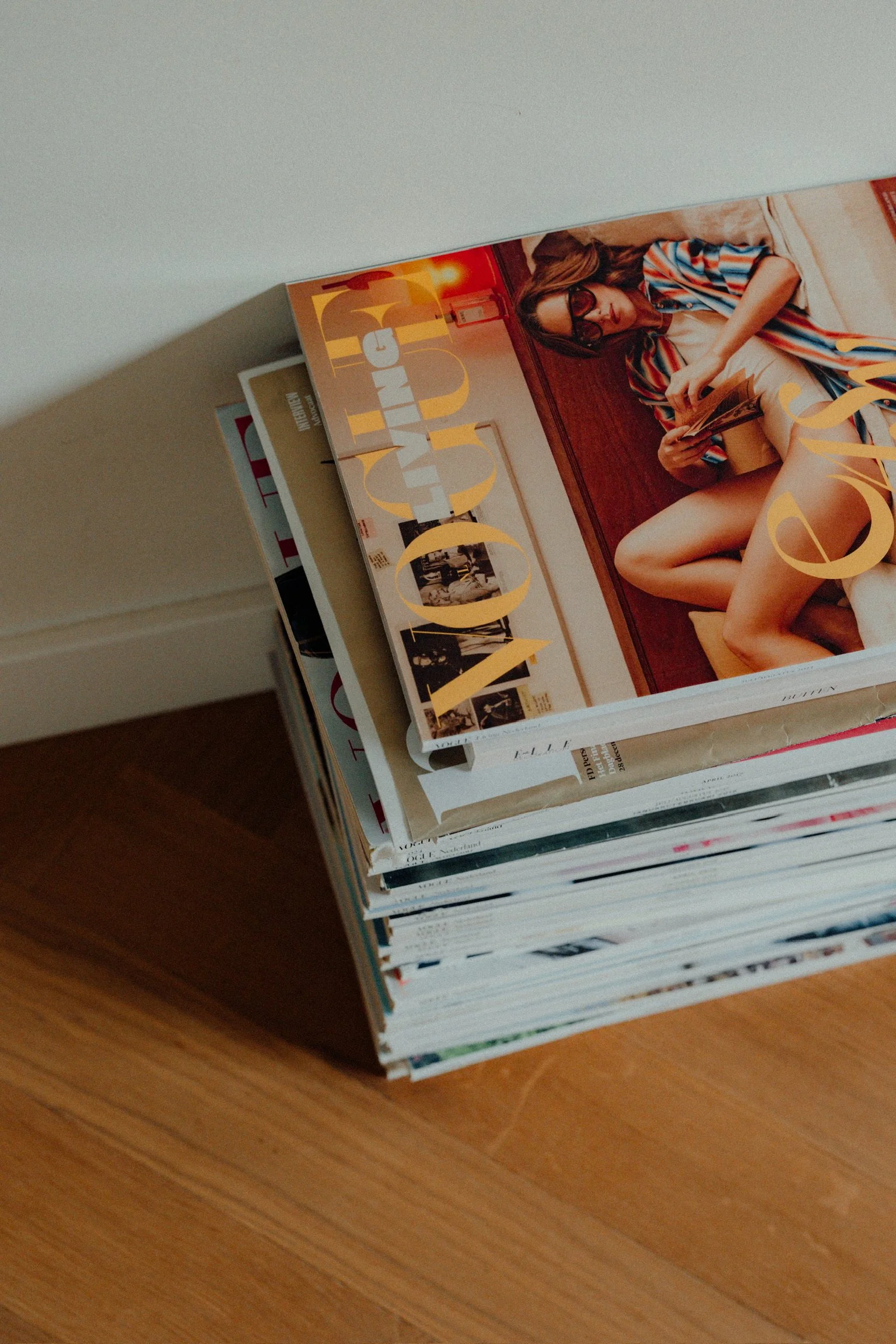 Een stapel tijdschriften ligt op een houten vloer, met de bovenste open en met een hand die erdoor bladert.