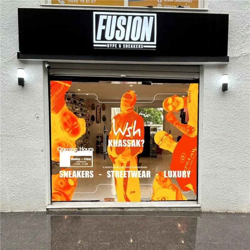 Store window with colorful graphics of people and text promoting sneakers, streetwear, and luxury items. The store name is Fusion, Hype & Sneakers. Opening hours are Monday to Friday from 12:00 to 21:00.
