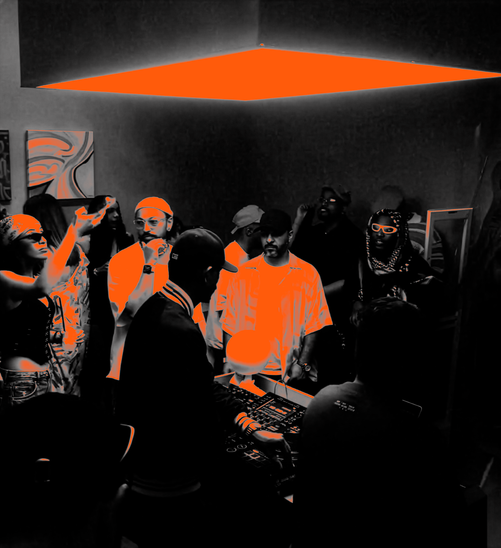 A group of people gathered in a room with a DJ controlling music equipment in the foreground. Some individuals are talking or wearing headphones, and the room has a dark background with an orange ceiling light.