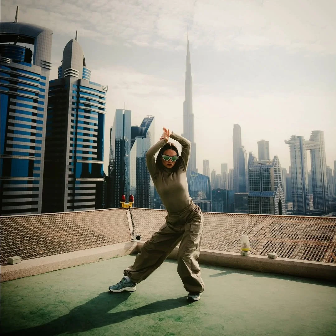 A woman dancing on a rooftop with a city skyline, including the Burj Khalifa, in the background.