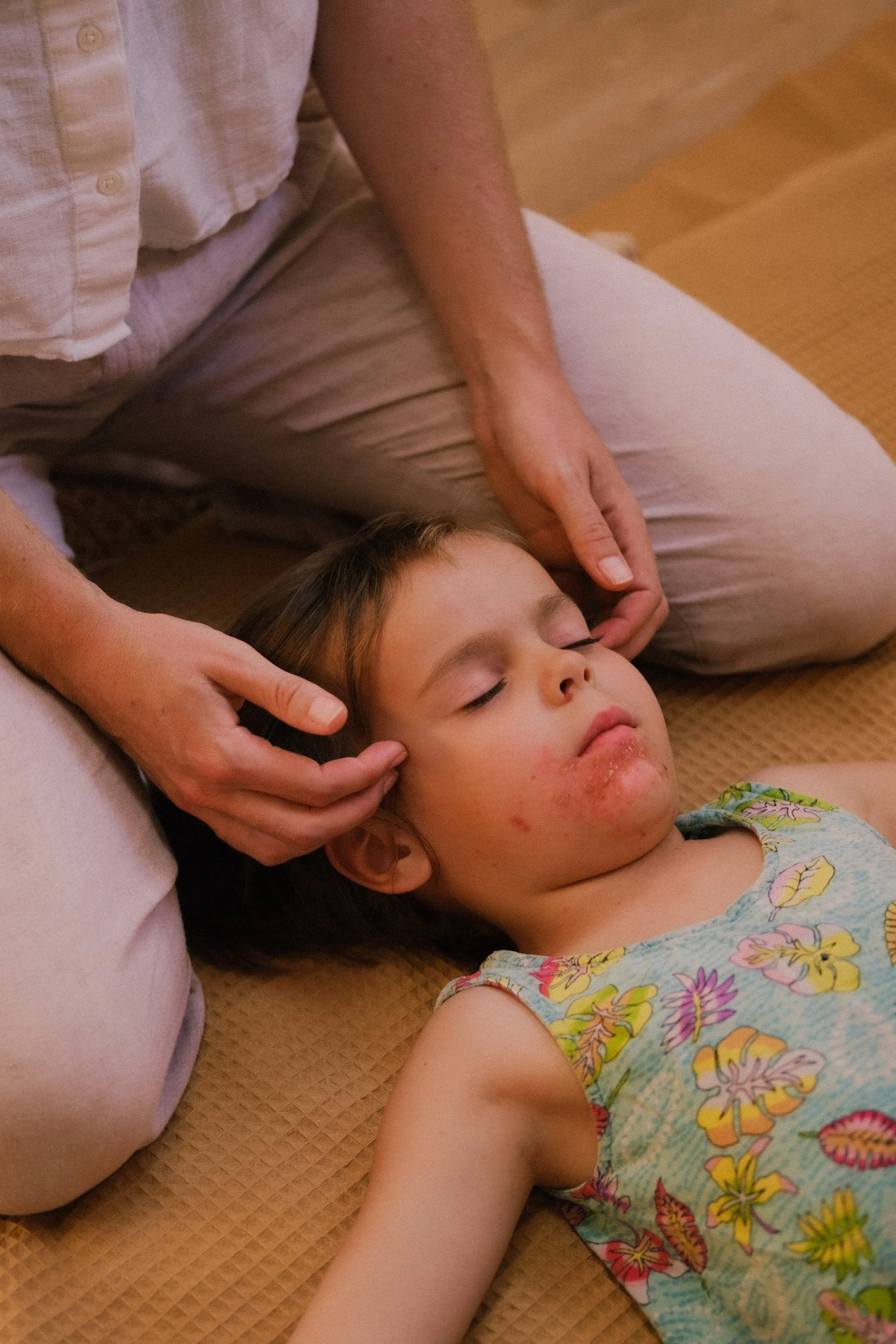 Jeune fille endormie sur le dos avec un visage apathique, portant un chemisier coloré avec des fleurs, allongée sur un tapis beige.