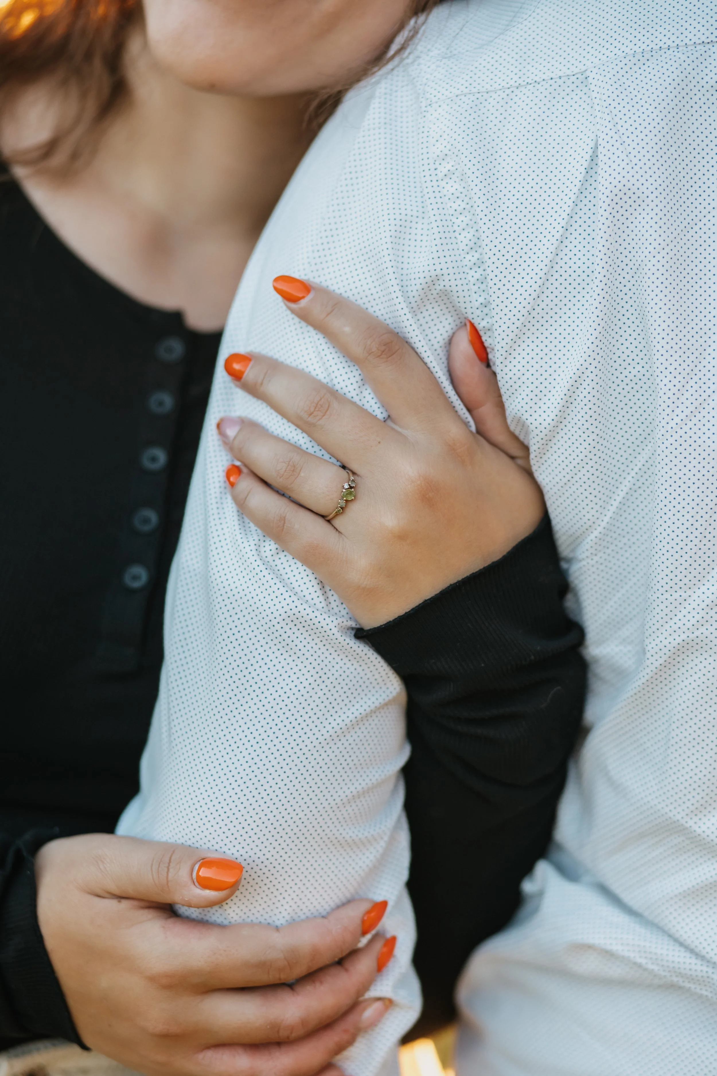 Nahaufnahme eines Menschen, der eine andere Person hält, beide tragen weiße und schwarze Kleidung. Die Person, die gehalten wird, hat orange Nagellack und trägt einen Ring.