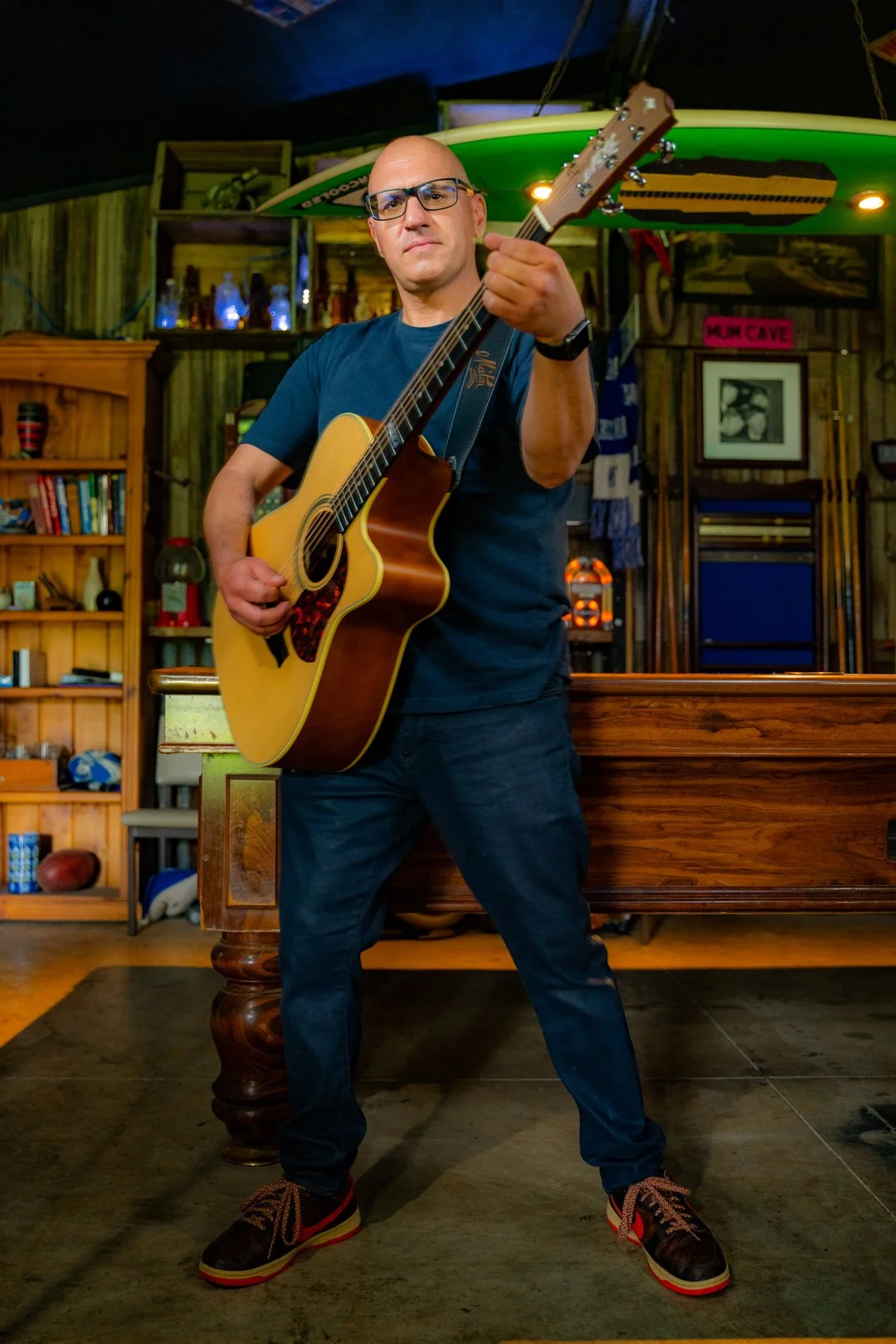 A man playing an acoustic guitar indoors in a bar or pub setting.