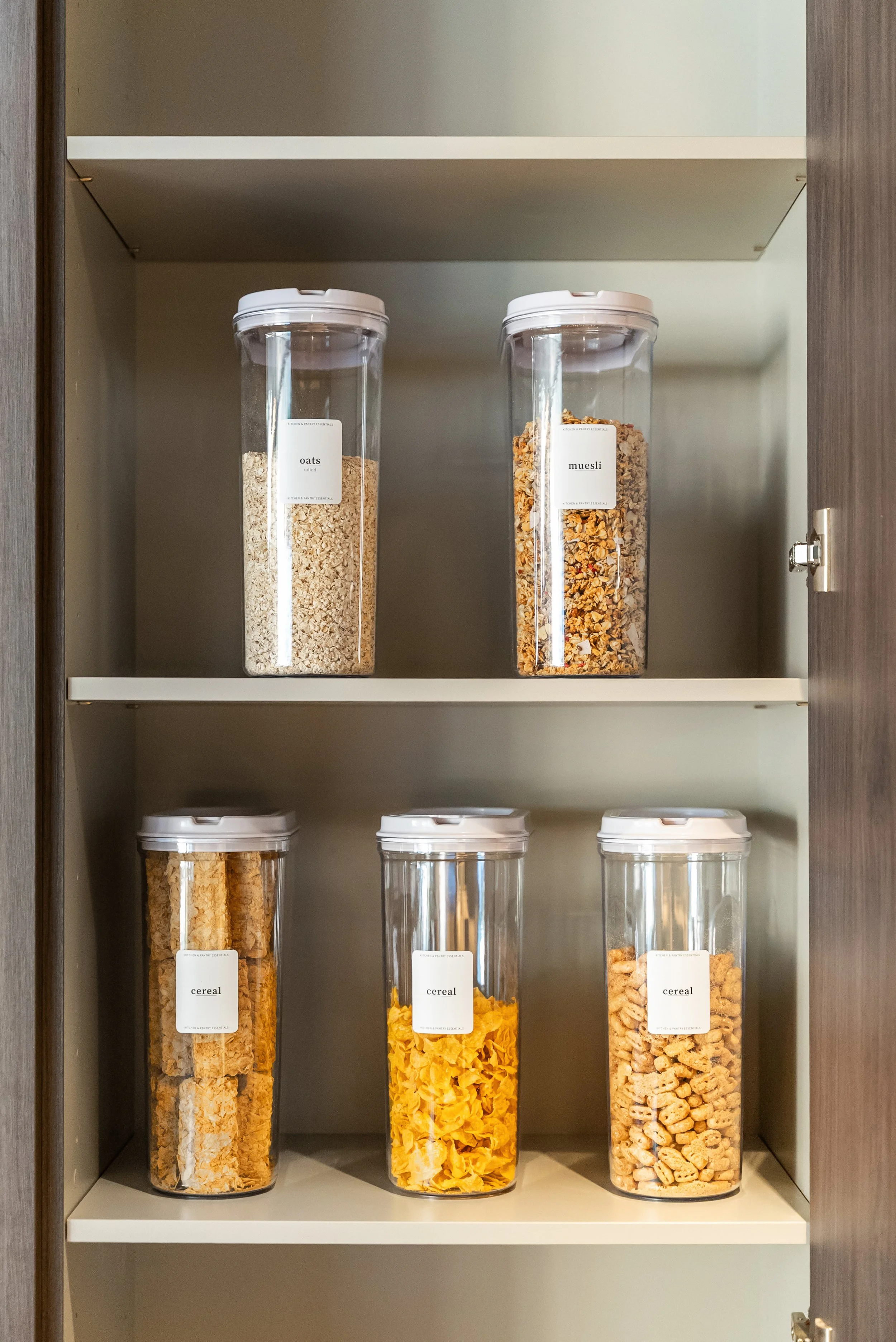 Pantry shelving with clear labelled canisters of decanted grains and cereals.