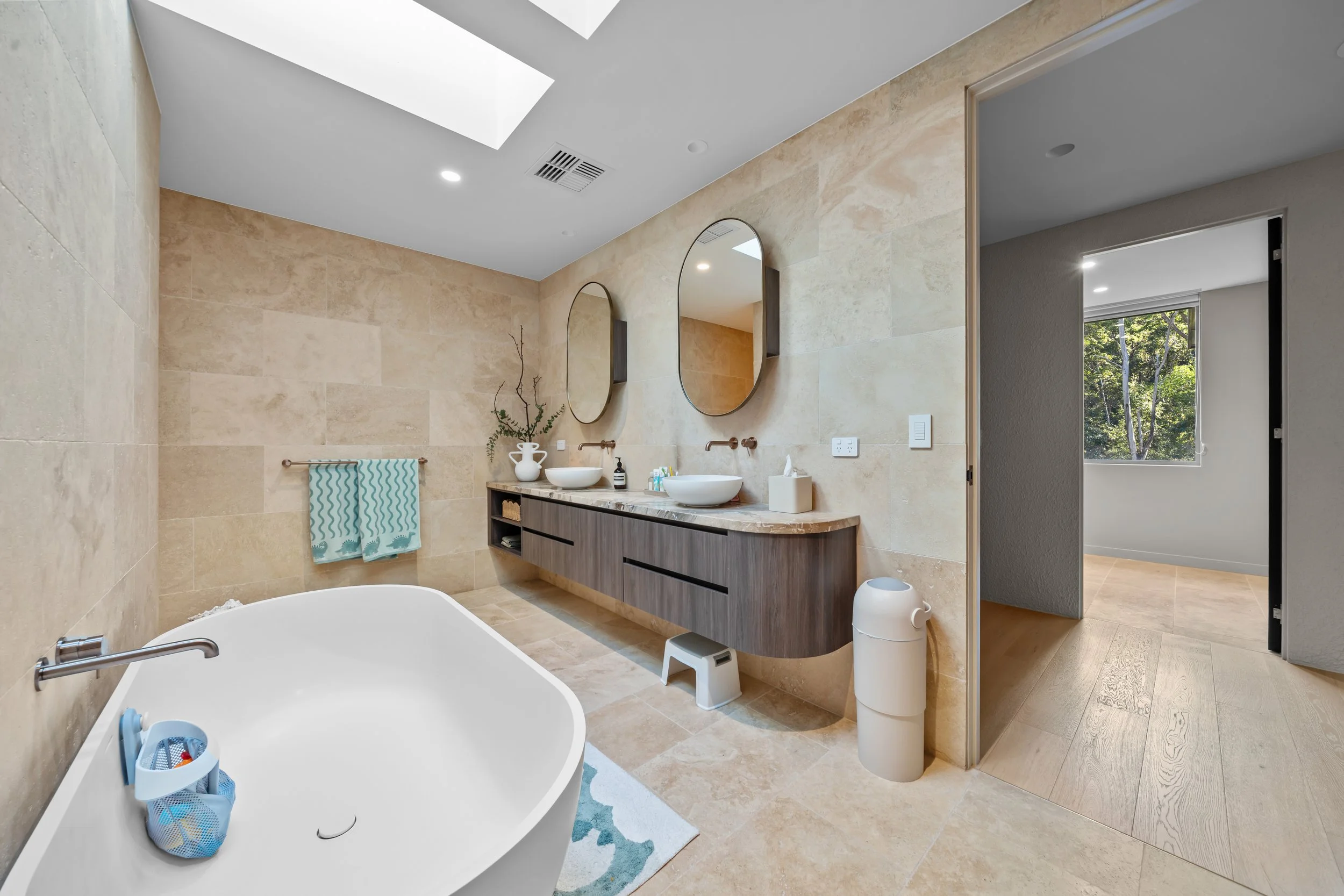 Bathroom with a freestanding tub, timber double vanity and round mirrors.