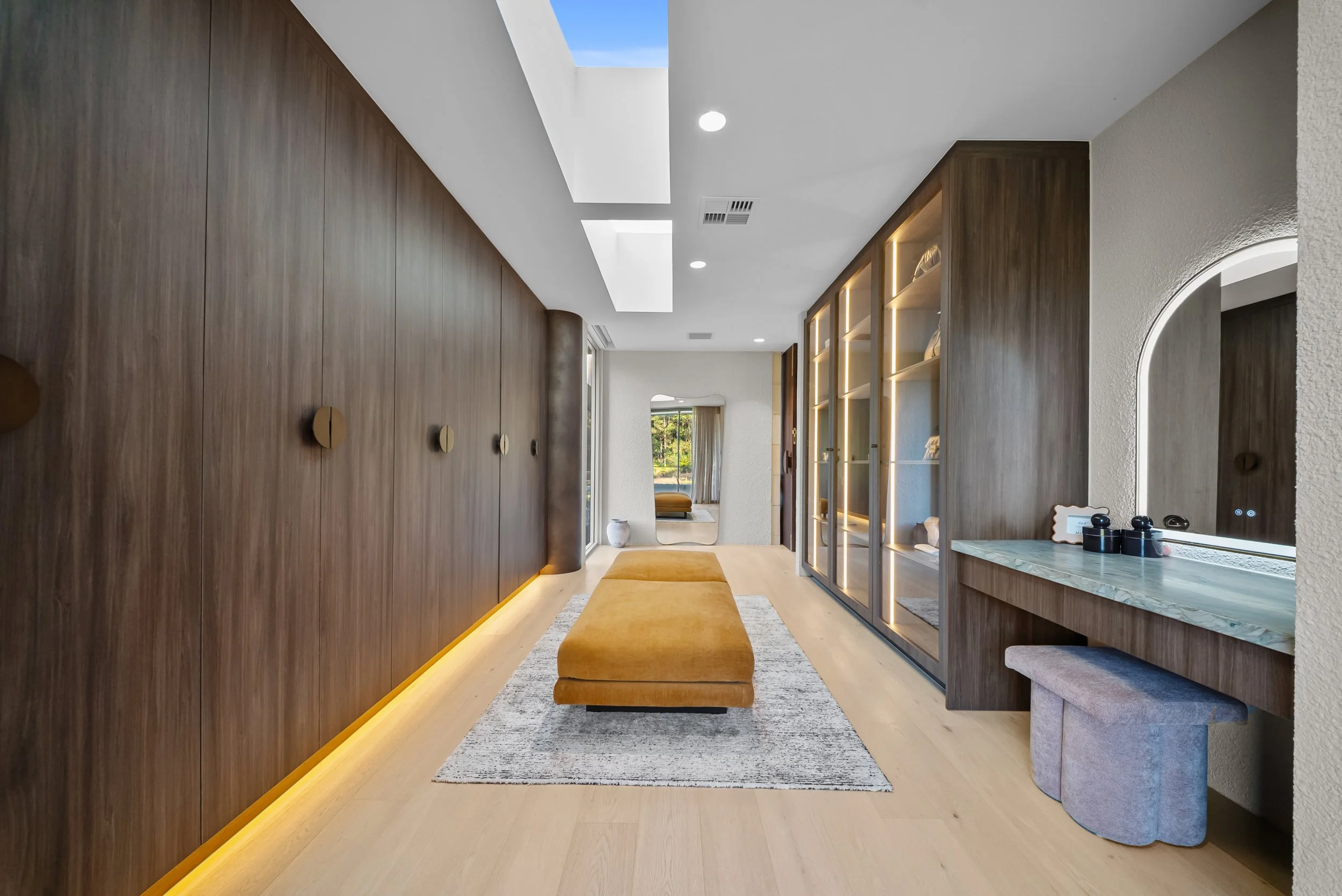 Warmly lit master wardrobe hallway with a timber bench and built-in cabinetry.