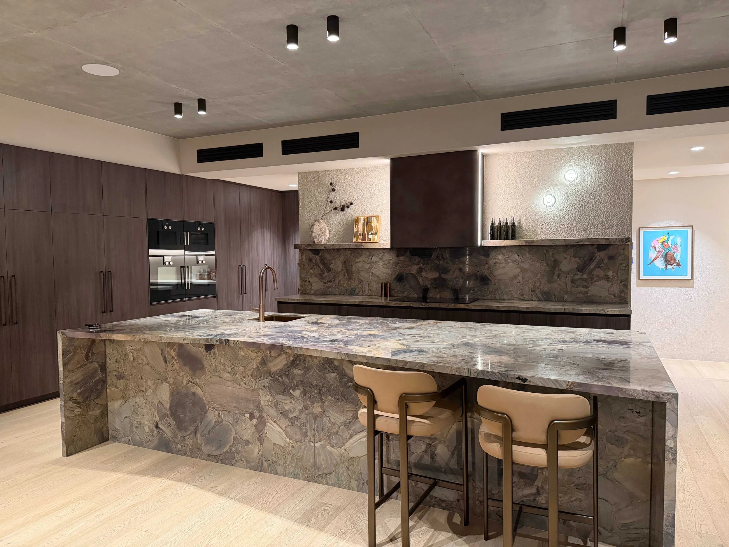 Organised open-plan kitchen at Stella Place with a large marble waterfall island, bar seating and integrated dark timber cabinetry.