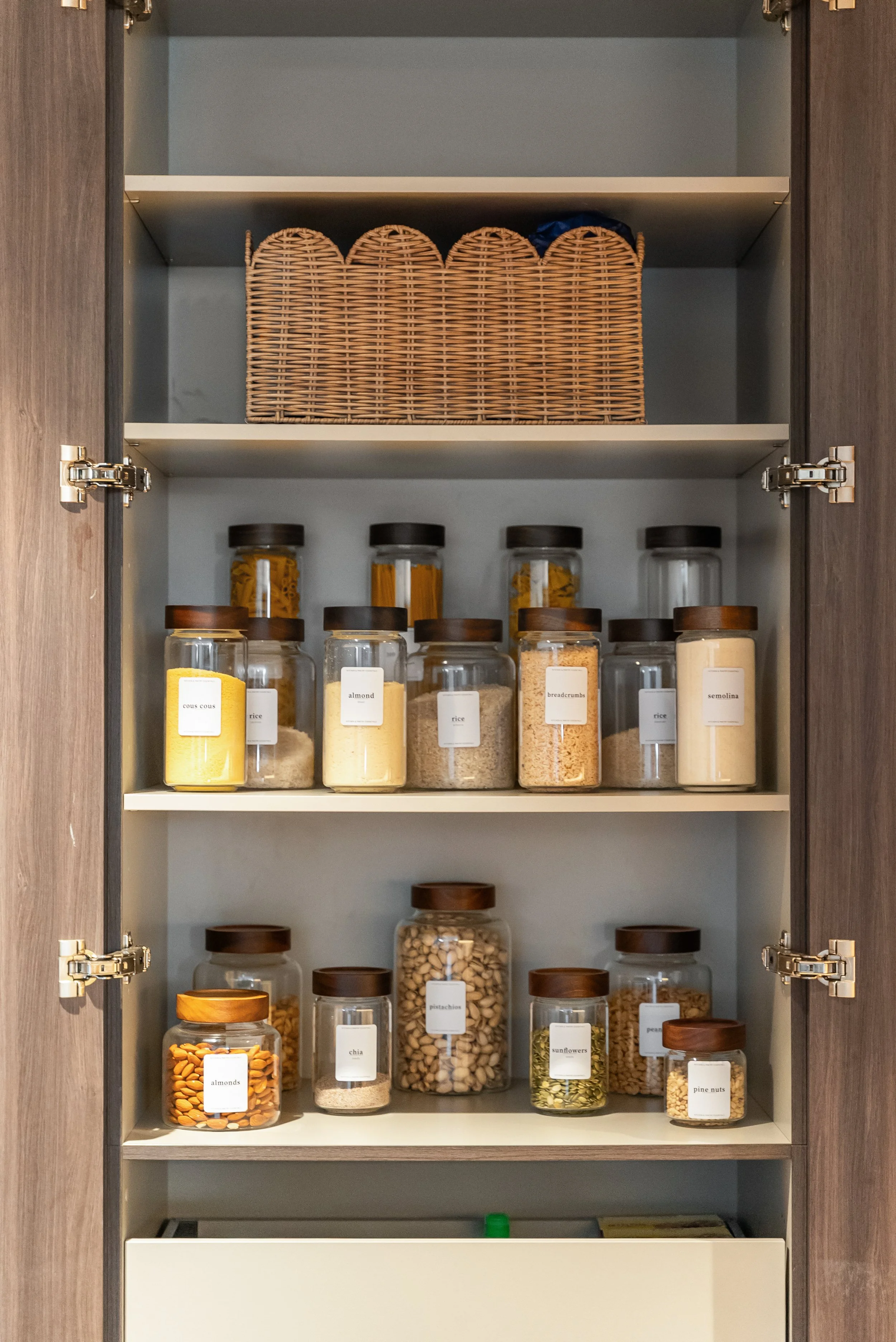 Pantry shelf with a woven backstock basket and rows of labelled jars.