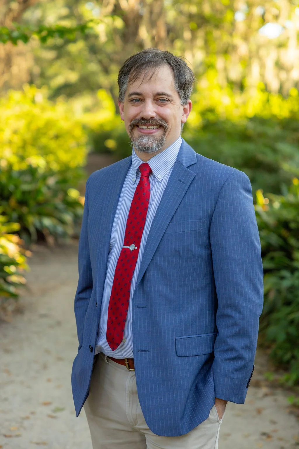 Joseph in blue suit with red tie with blurred greenery in background